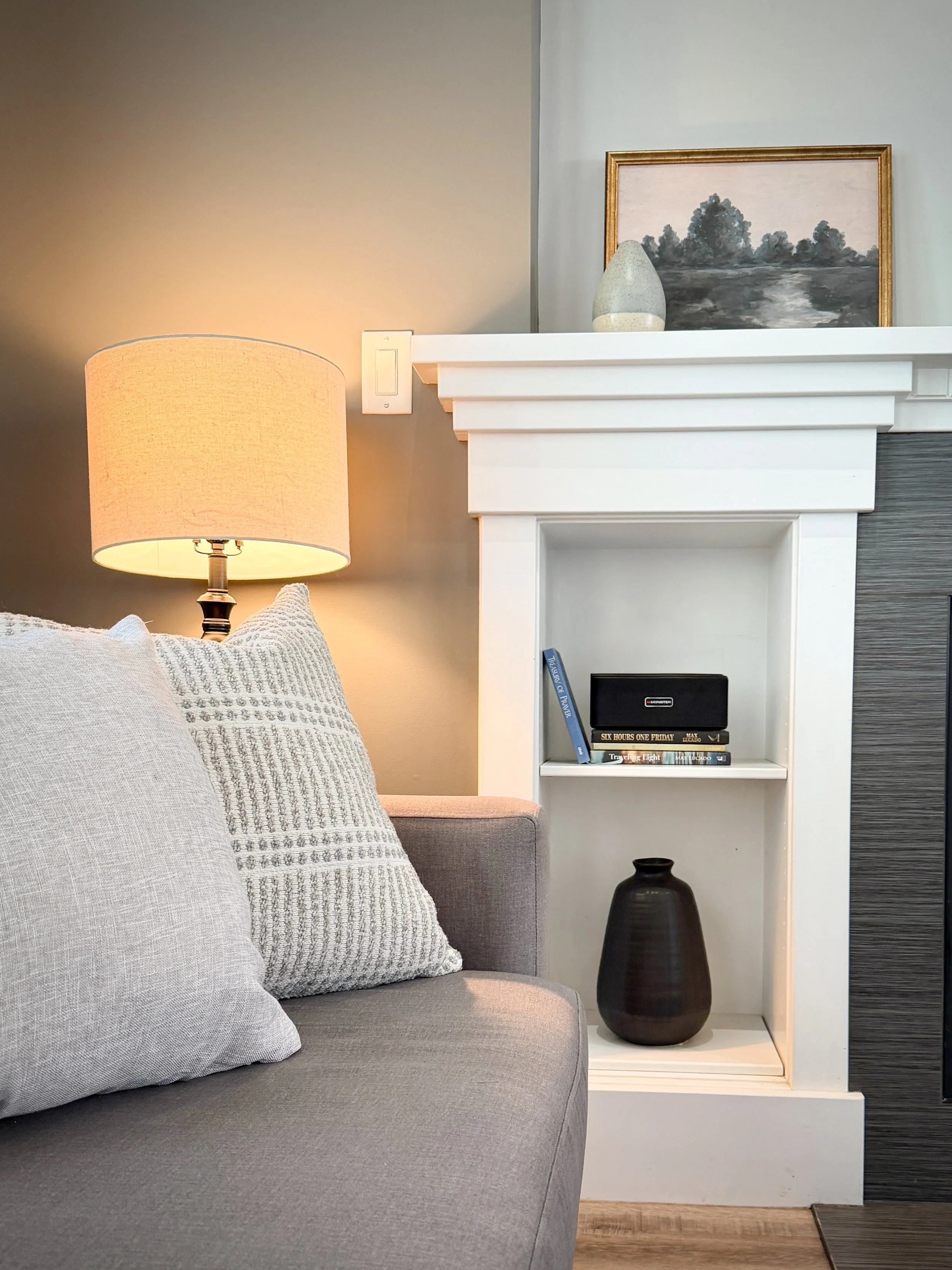 A light filled living room with a grey sofa, lamp and small art.
