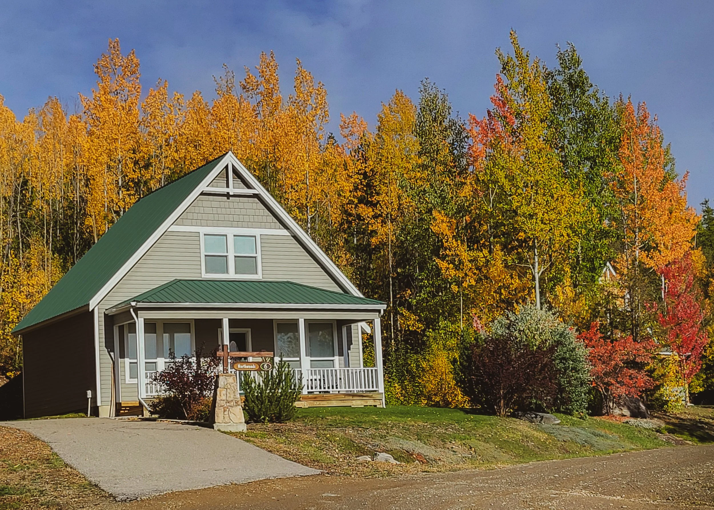A small cottage with a porch in trees that are yellow, red and orange in the fall.