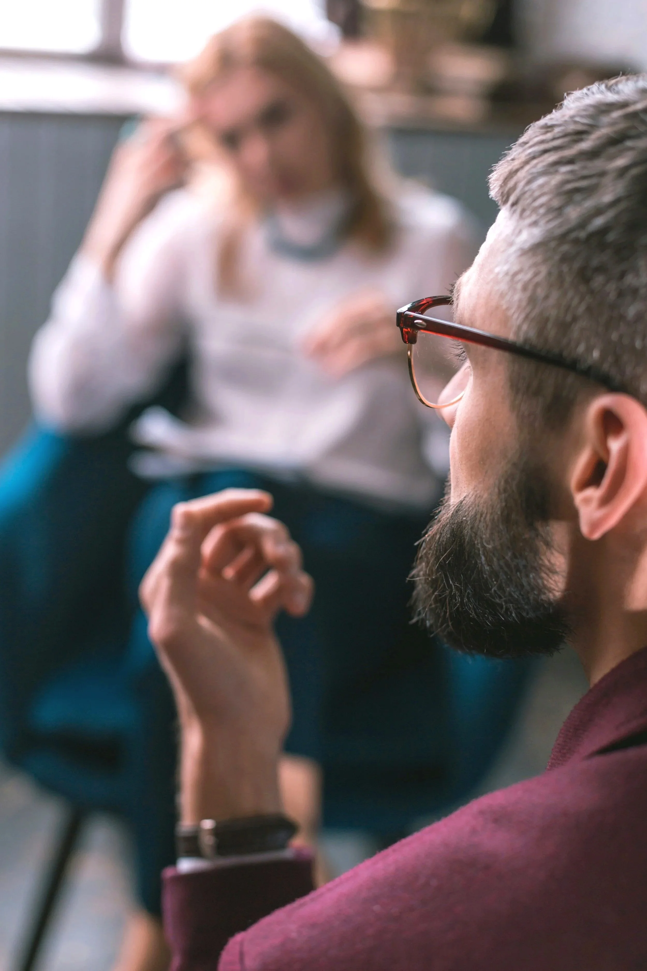 Two people engaged in conversation, one wearing glasses, in a casual indoor setting.