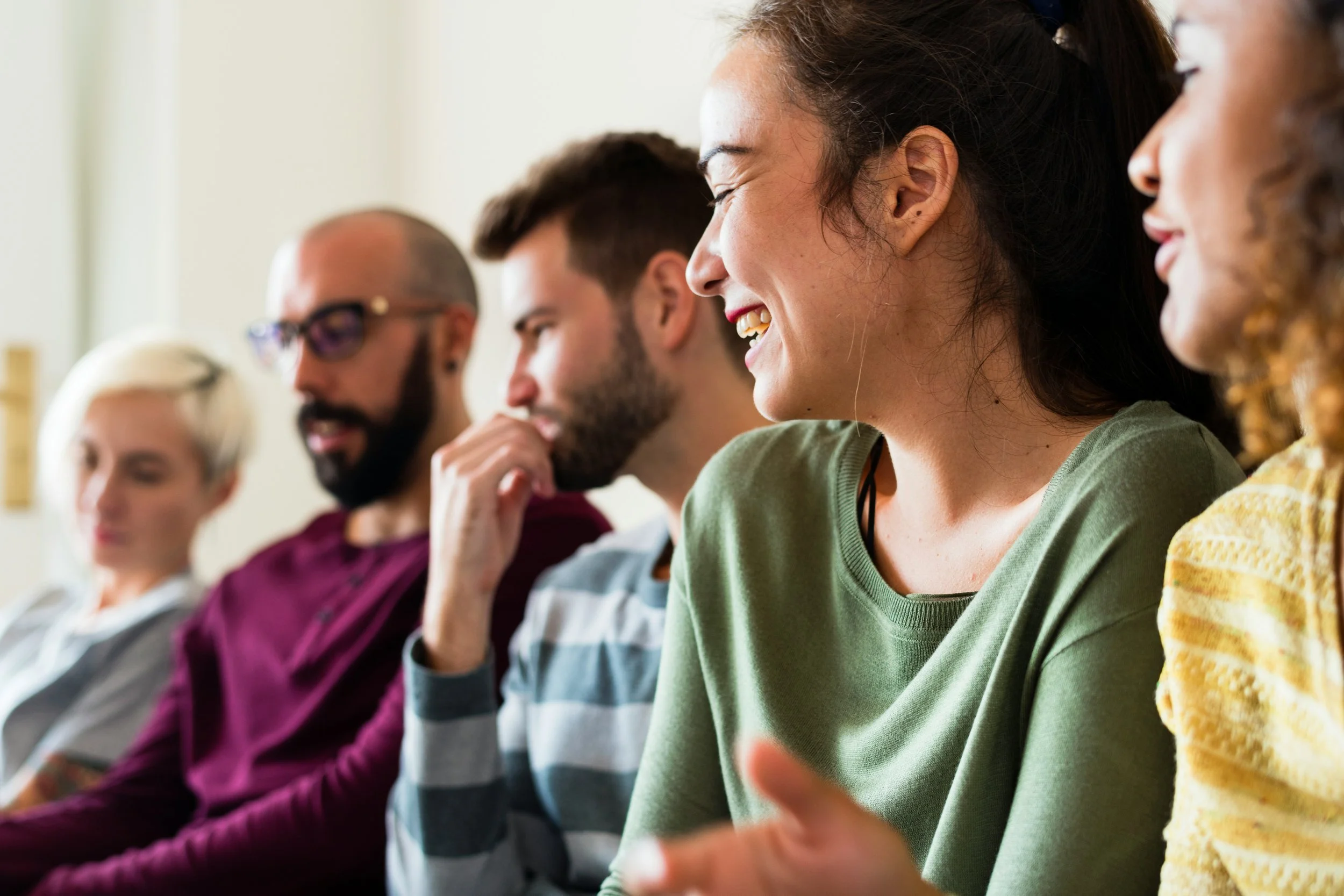 People sitting in a row during a meeting or event, smiling and engaging with each other.