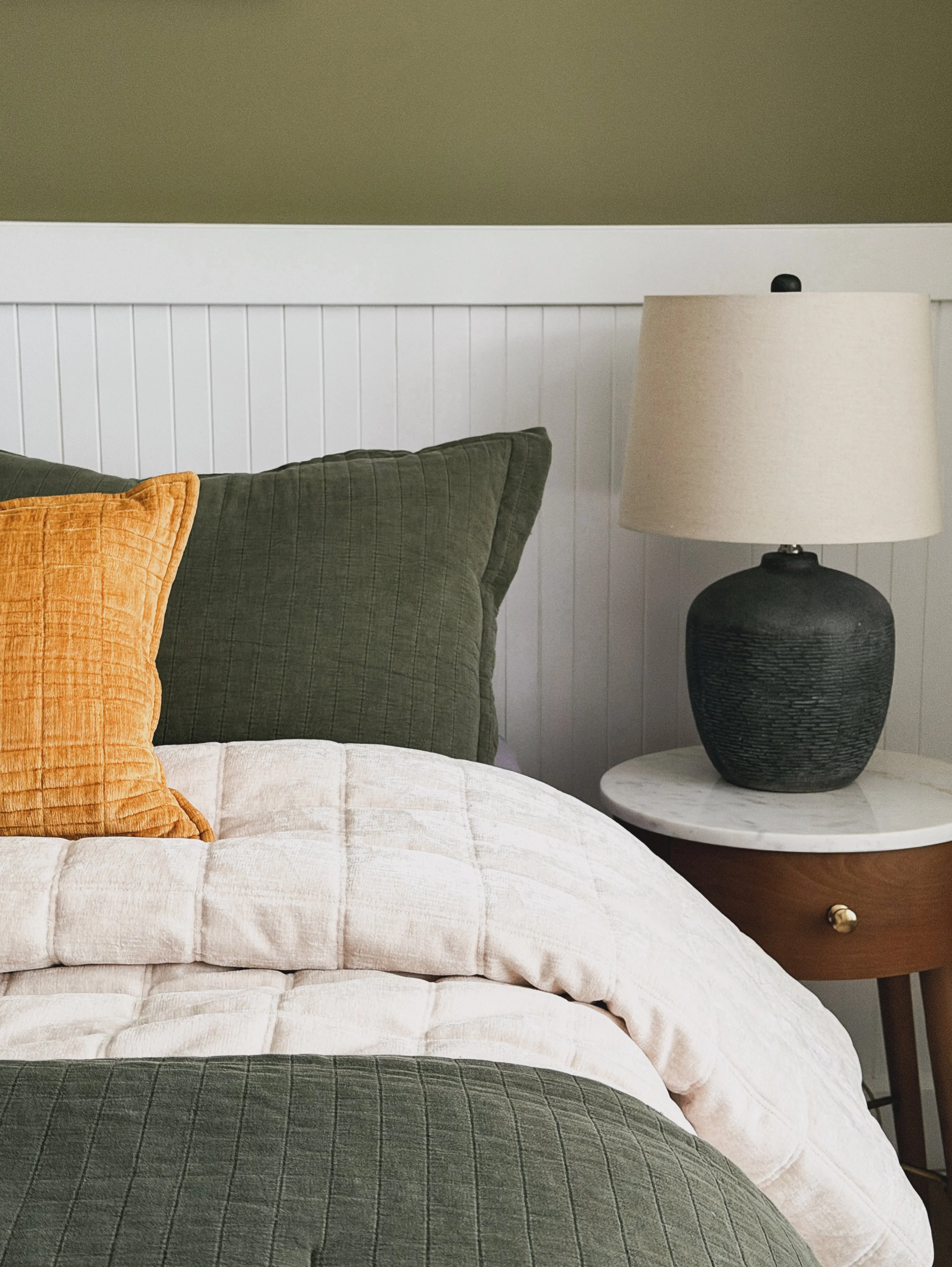 A bed with green and yellow pillows, green walls and a black lamp.