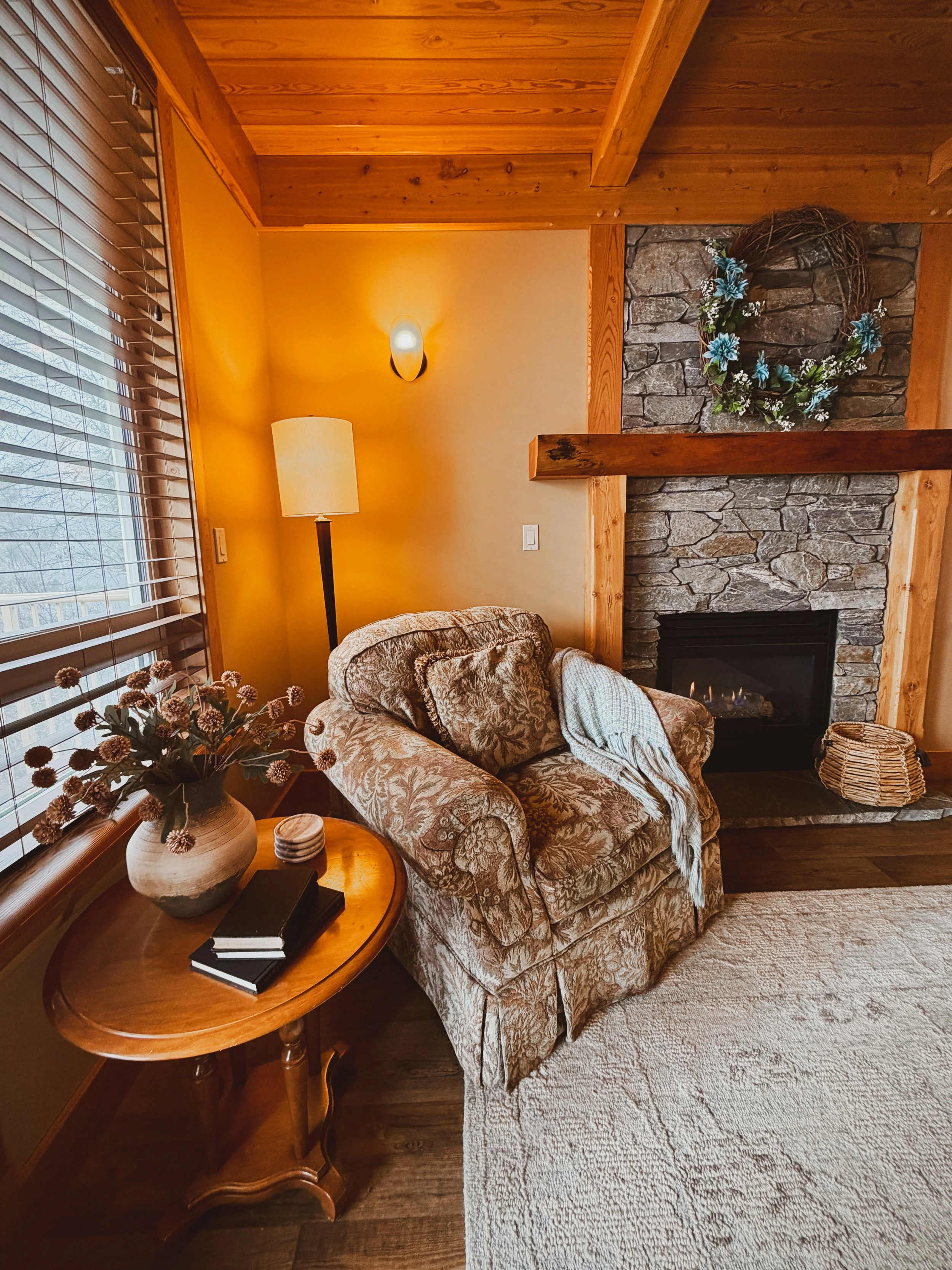 A cosy chair in a cottage with a stone fireplace and wooden beams and ceiling.
