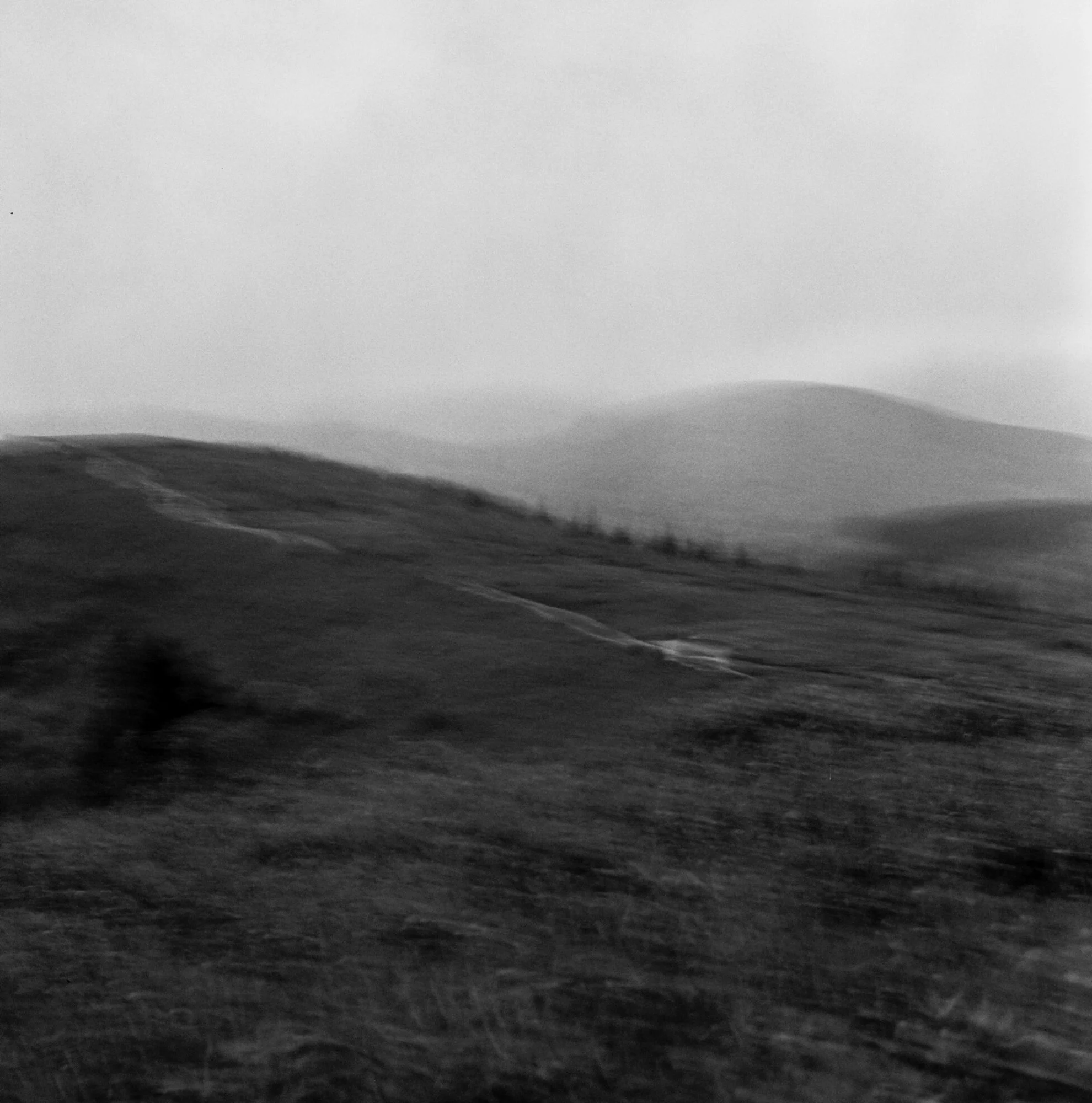 Black and white photograph of a landscape with rolling hills and a cloudy sky.