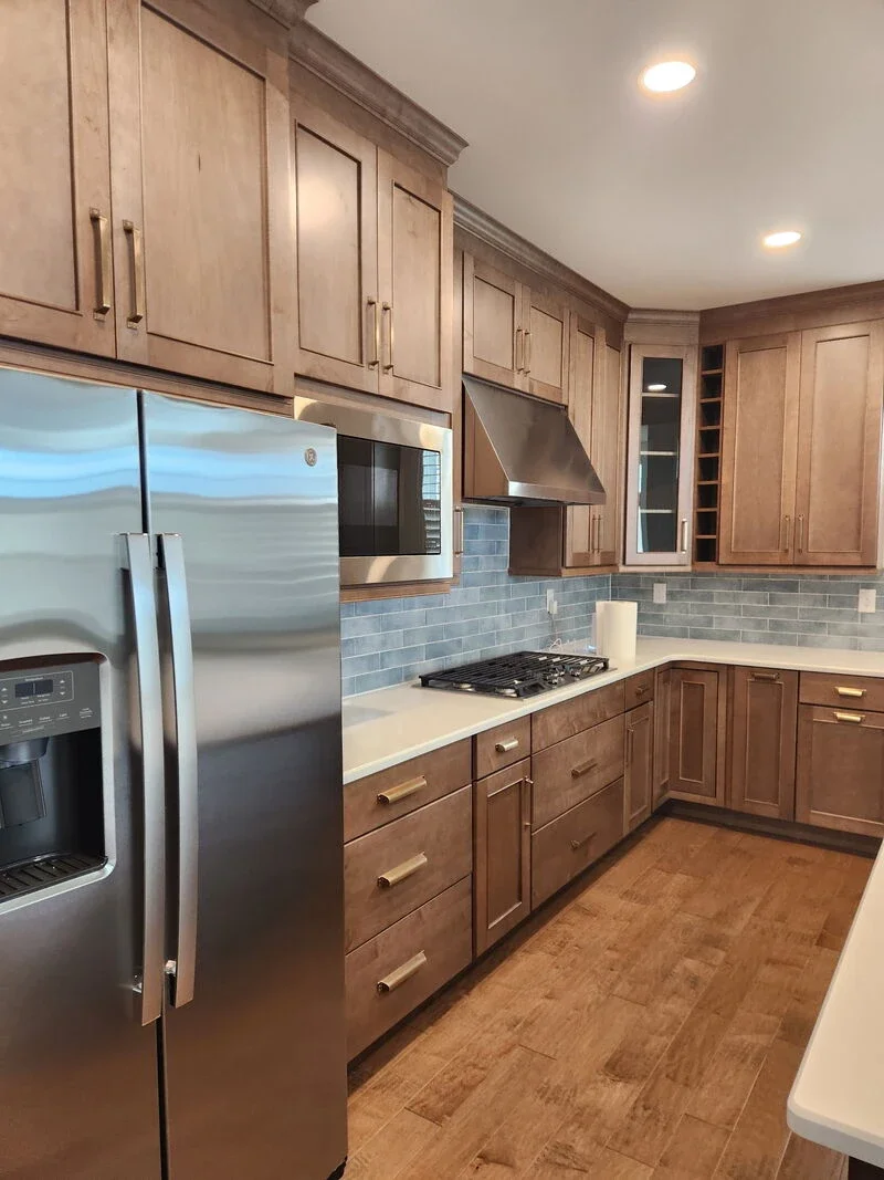 Modern kitchen with wooden cabinets, stainless steel refrigerator, microwave, gas stove, stainless steel range hood, and blue tile backsplash.