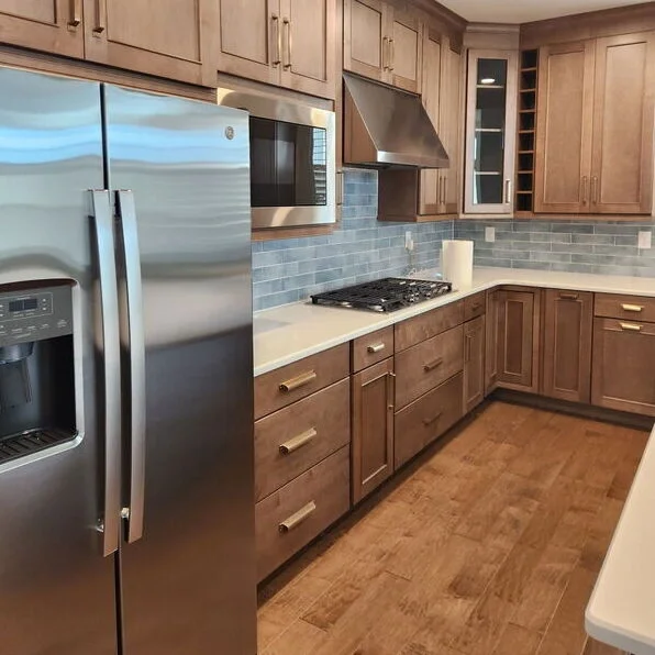 Kitchen with stainless steel refrigerator, microwave, gas stove, wooden cabinets, gray tile backsplash, and wooden flooring.
