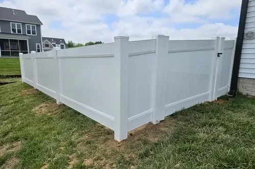 White privacy fence surrounding a yard with green grass and neighboring houses visible in the background.