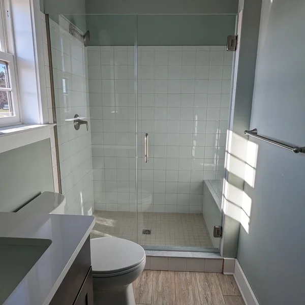 A bathroom with a glass-enclosed shower, a toilet, a small vanity with a sink, and a window letting in natural light.