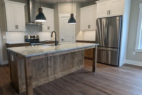 Modern kitchen with white cabinets, stainless steel refrigerator, granite island, and pendant lighting.