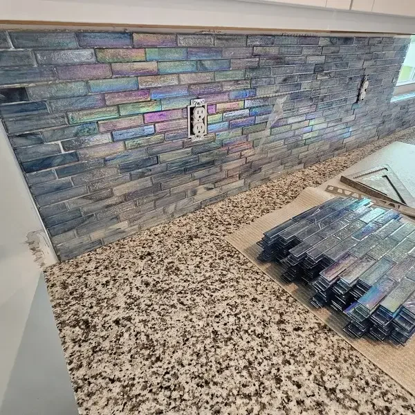 A kitchen backsplash installation with iridescent blue and purple tiles