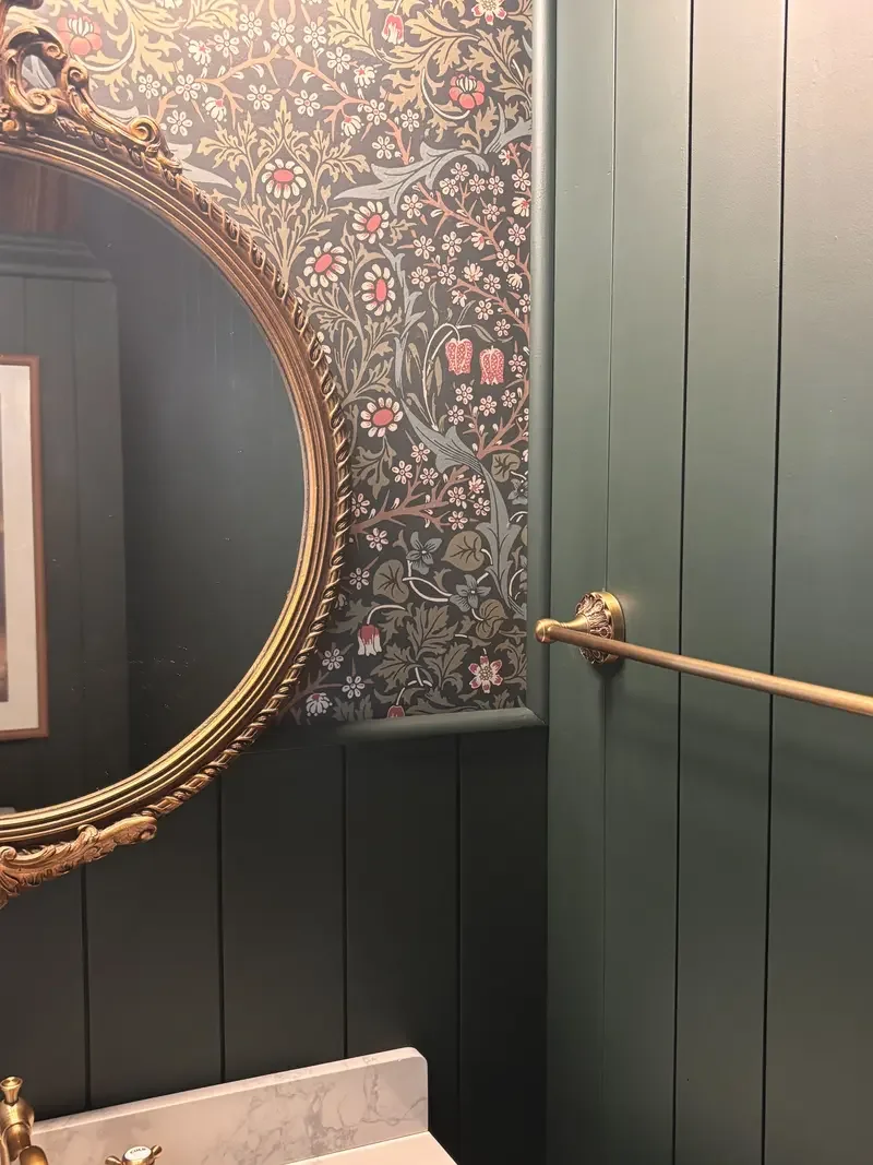 Renovated bathroom: Decorative bathroom interior with a large ornate gold-framed mirror, floral wallpaper, and green wooden panel walls, with a gold towel rack. Milford, DE