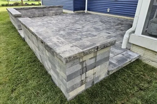 Gray concrete block patio with a step leading to a house with blue siding and white trim.