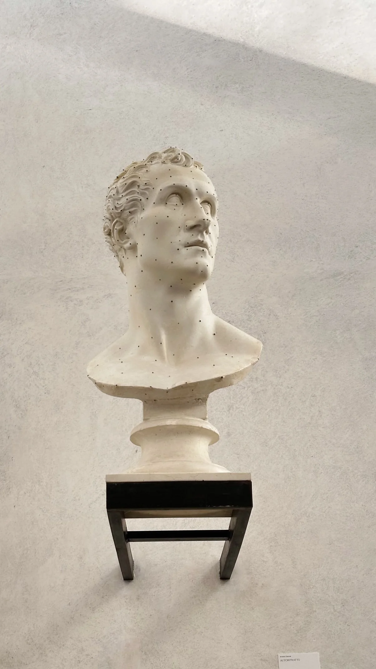 Marble bust sculpture of a man with curly hair, placed on a pedestal in an art gallery.