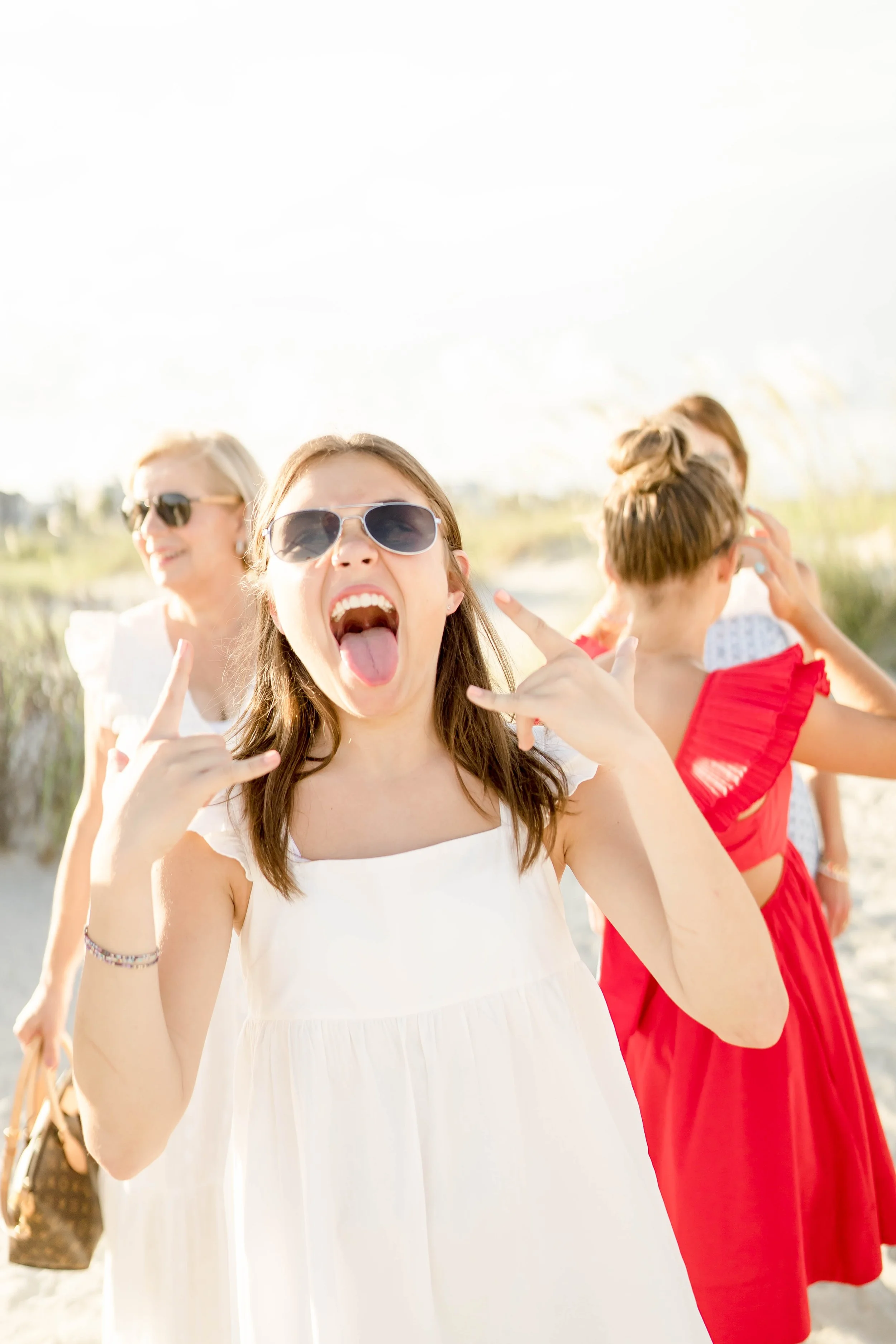 Group of women at the beach, one wearing sunglasses and sticking her tongue out.