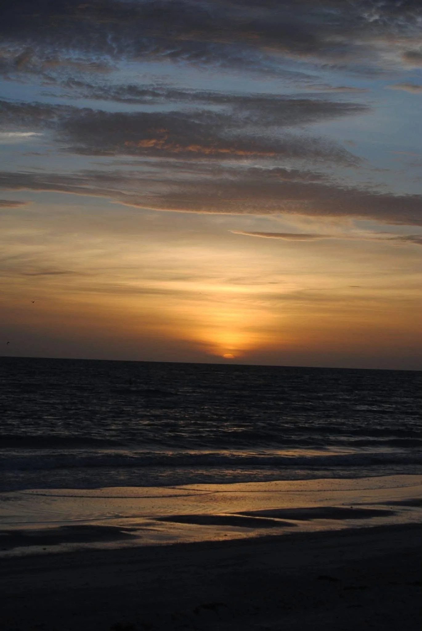 A sunset over the ocean with dark clouds in the sky and gentle waves on the beach.
