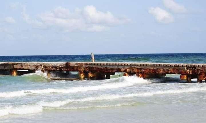 A weathered wooden pier extending into the ocean with waves crashing near the shore.