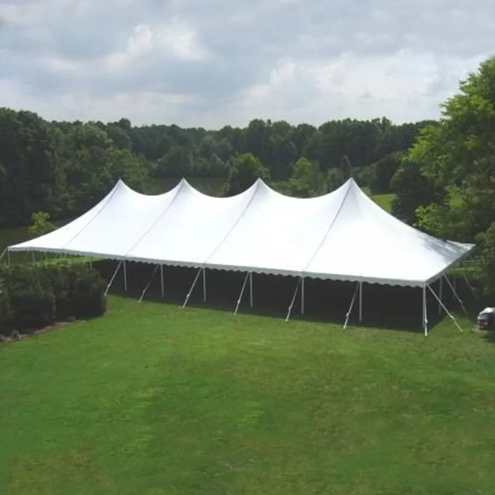 A large white event tent set up on a grassy lawn near a body of water, surrounded by trees under a cloudy sky.