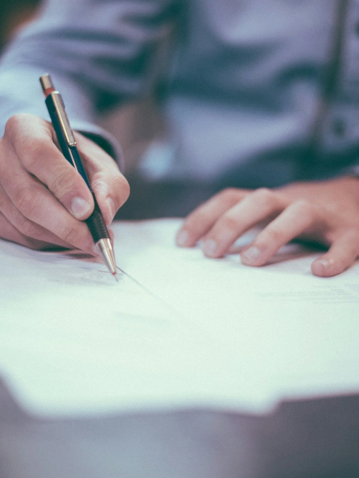 A person signing a roofing insurance claim with a pen, with only their hand and part of their arm visible.