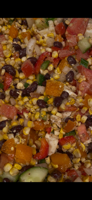 Close-up of a colorful mixed salad with corn, black beans, diced tomatoes, cucumbers, and chopped vegetables.