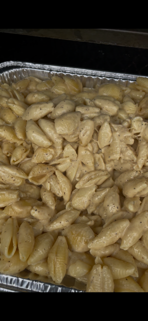Baked pasta shells with creamy cheese sauce in aluminum tray.