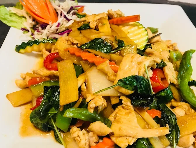 Stir-fried vegetables with chicken on a white plate, including bell peppers, zucchini, carrots, and spinach, served with a side of salad.