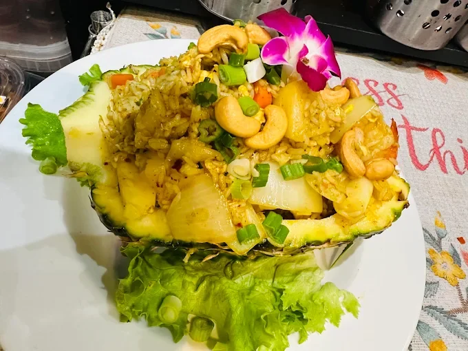 Pineapple boat filled with fried rice, garnished with cashews, green onions, and an orchid flower, on a white plate with lettuce.