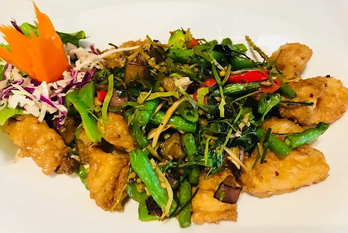 Fried fish fillets topped with fresh green vegetables and herbs, served with shredded vegetables and garnished with a carved vegetable flower.