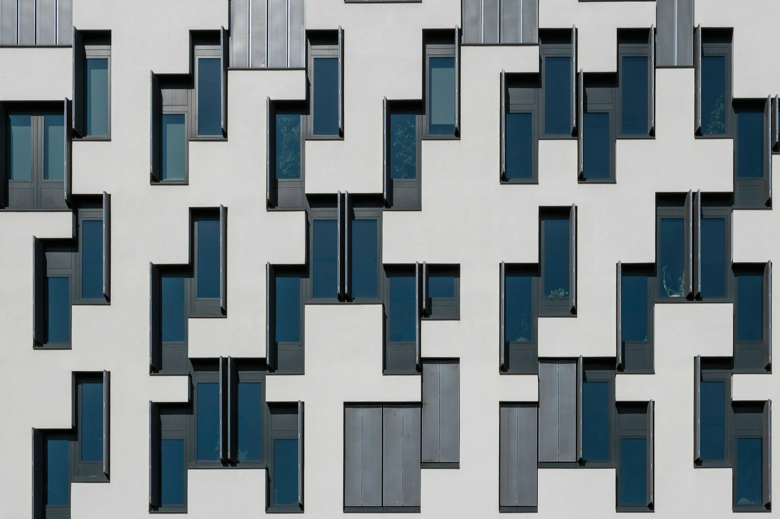 Modern building facade with numerous vertical windows and alternating sections of white and gray exterior walls.