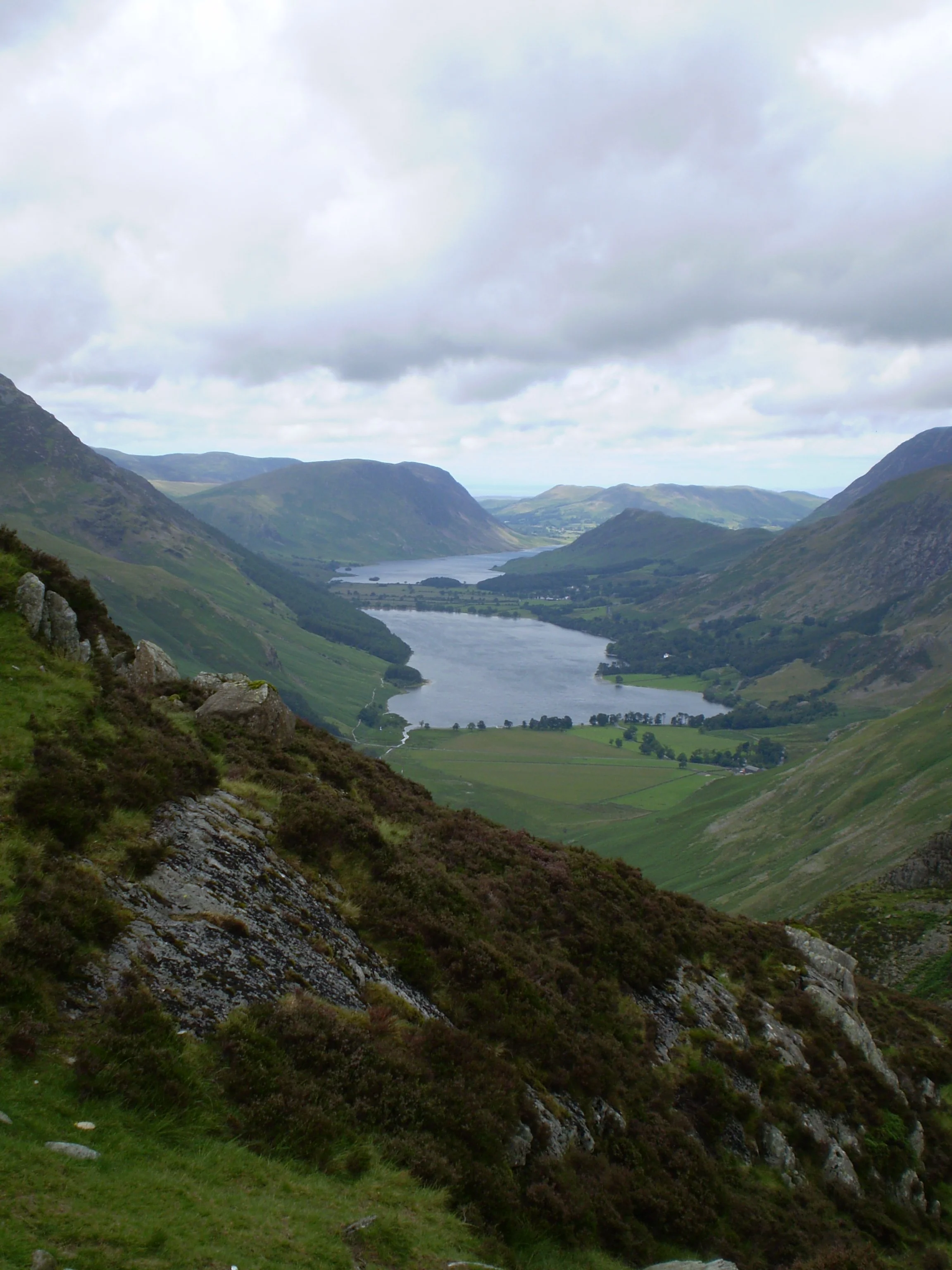 A valley with lush green hills and a winding river flowing through it, under a cloudy sky.