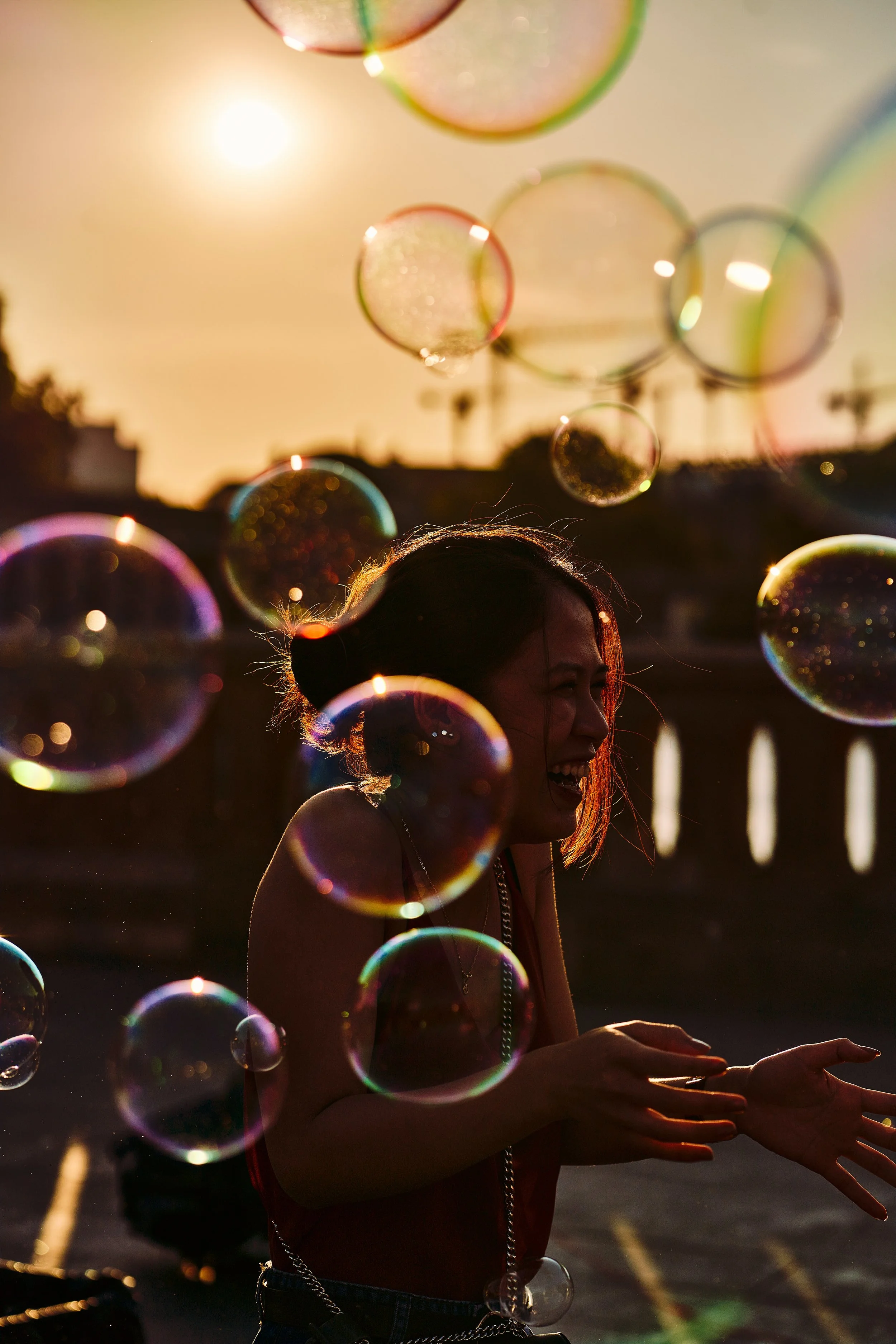 A woman smiling and playing with soap bubbles during sunset in an outdoor setting.