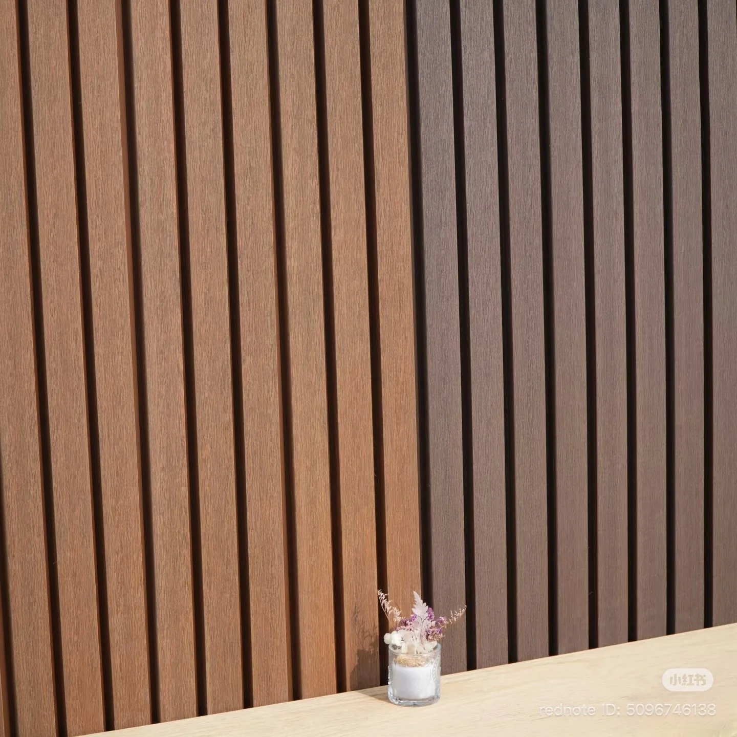 Small flower arrangement in a clear glass jar on a wooden surface with a wooden slat wall background.