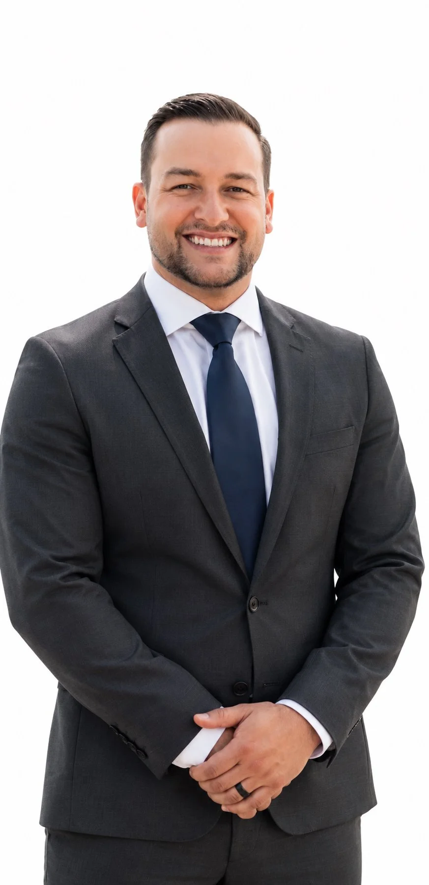 A smiling man in a dark gray business suit, white shirt, and navy tie, standing against a plain white background.