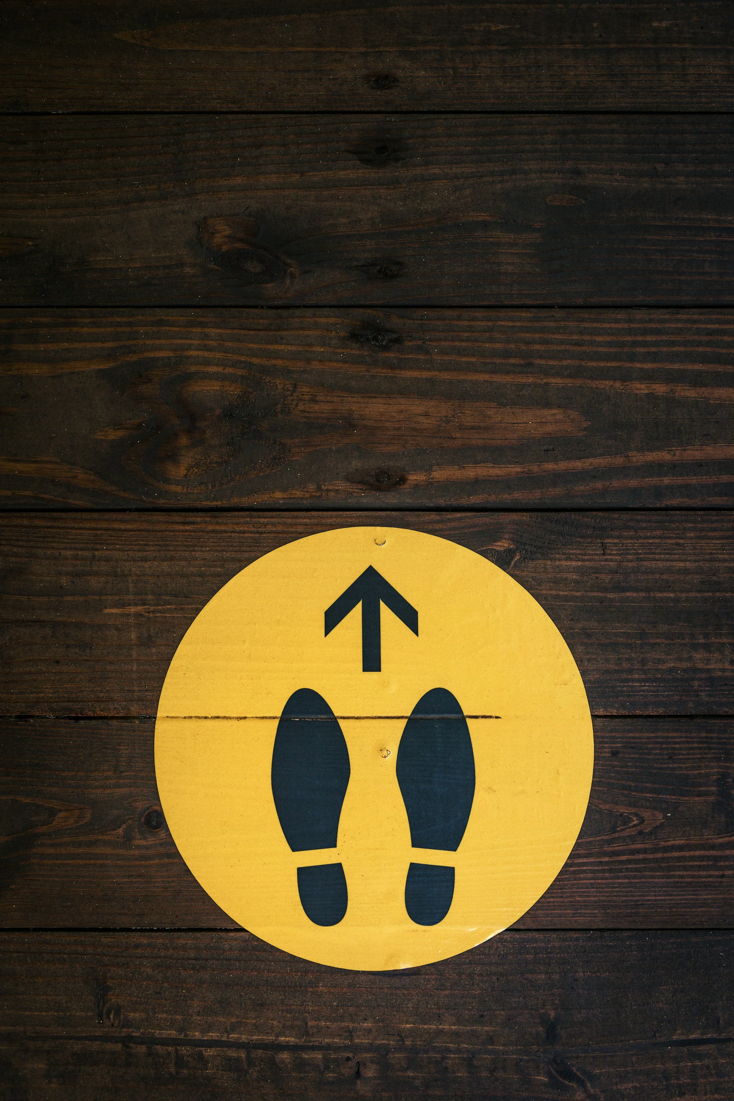 A yellow circle with two black shoe prints and an arrow pointing up is shown against dark brown hardwood.