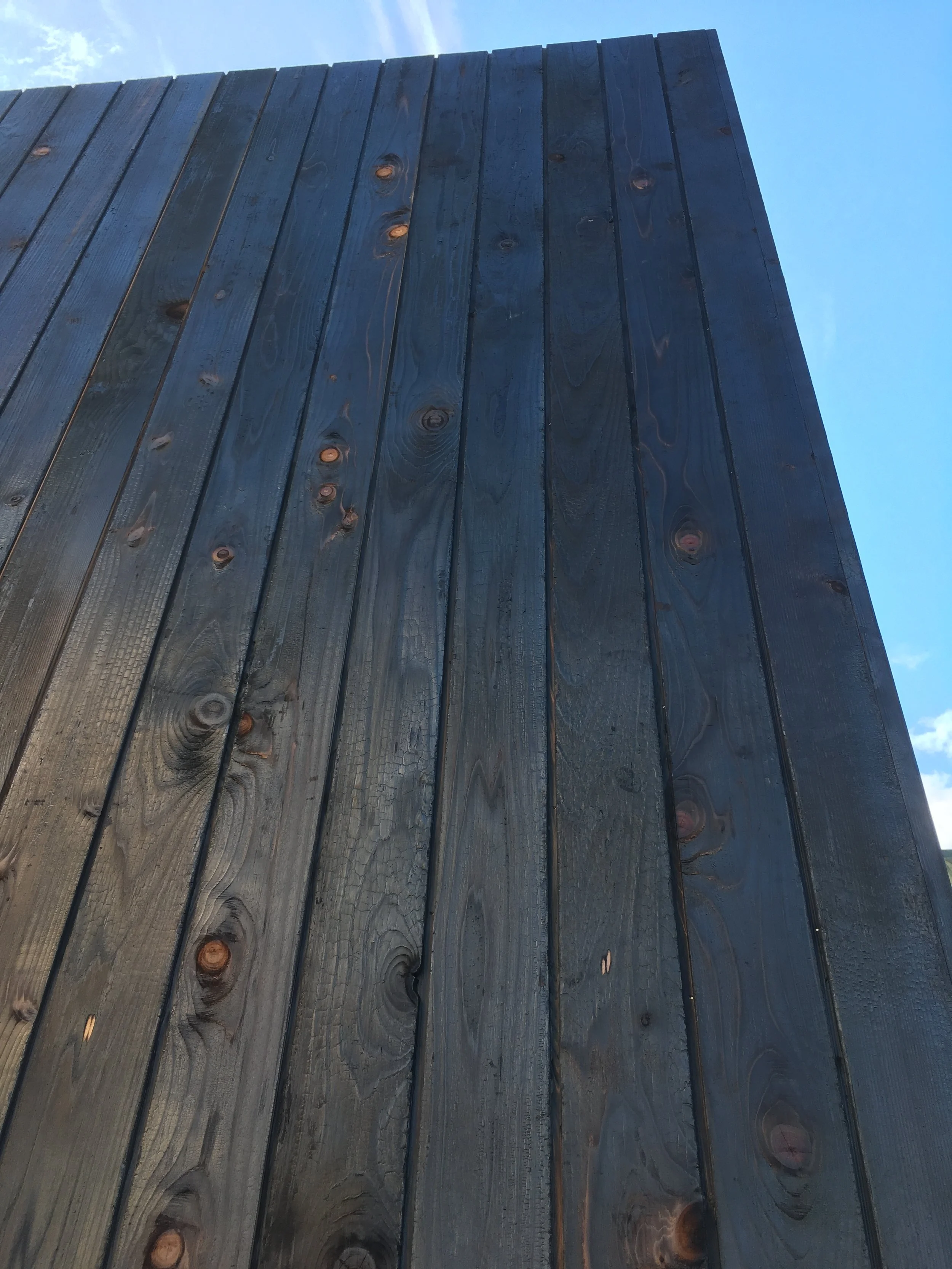 Close-up of dark stained wooden plank wall against a partly cloudy sky.