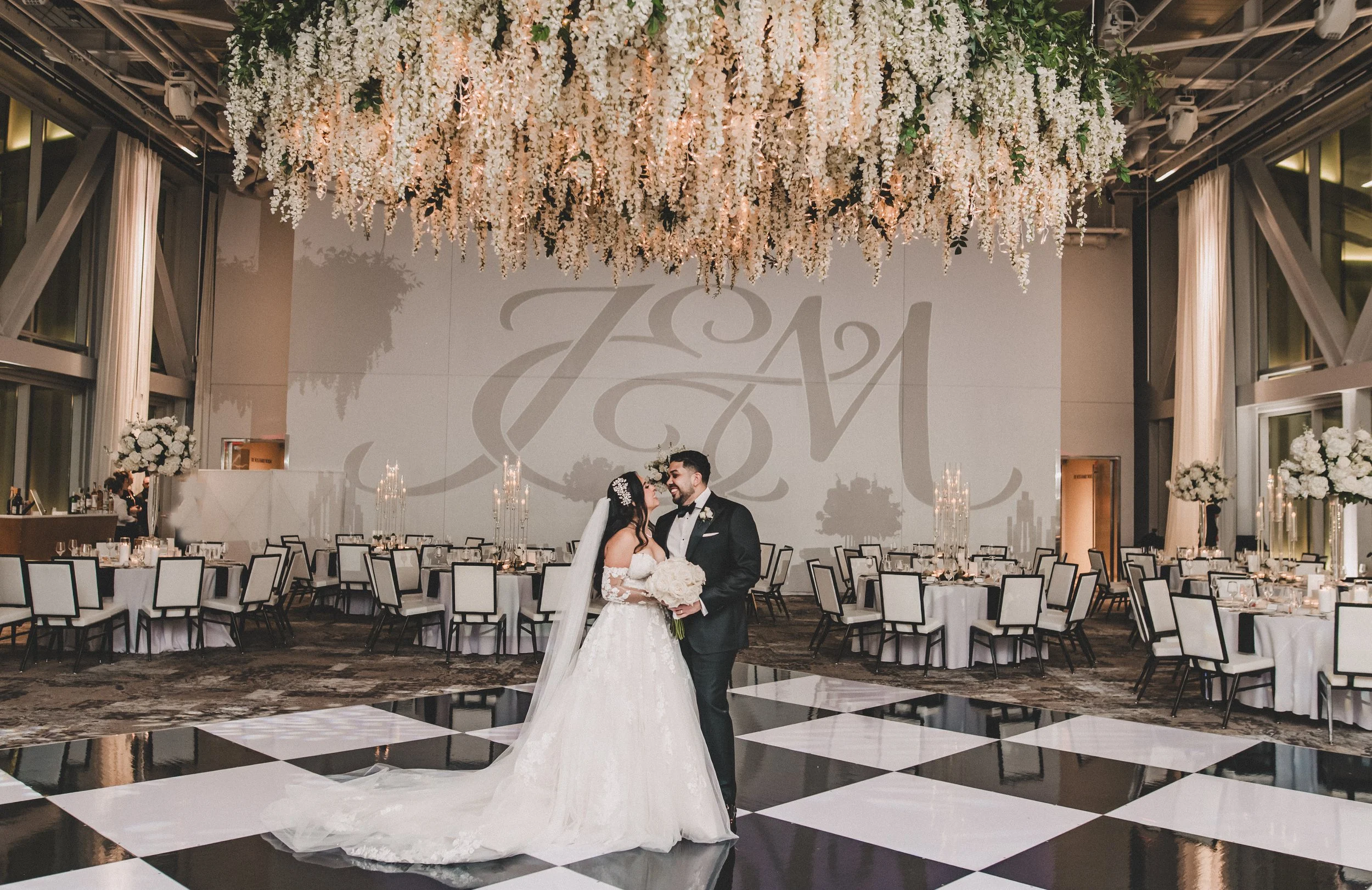 Bride and groom sharing a kiss at their wedding reception, decorated with white floral ceiling installation and elegant table settings in a modern event hall.