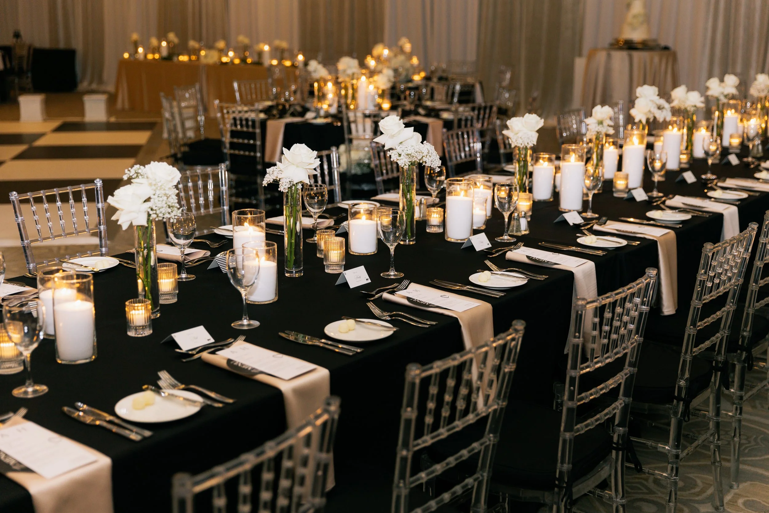 Elegant banquet table setup with white floral centerpieces and lit candles in tall and short glass holders.