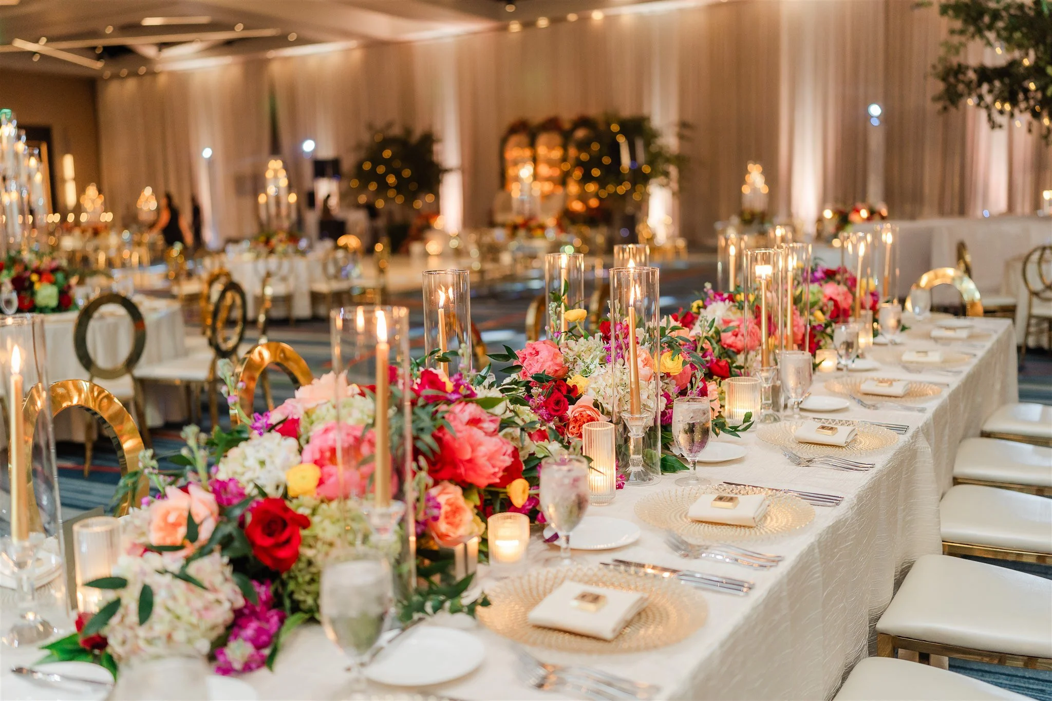 Elegant banquet setup with long tables adorned with vibrant floral centerpieces and lit candles, in a decorated event hall.