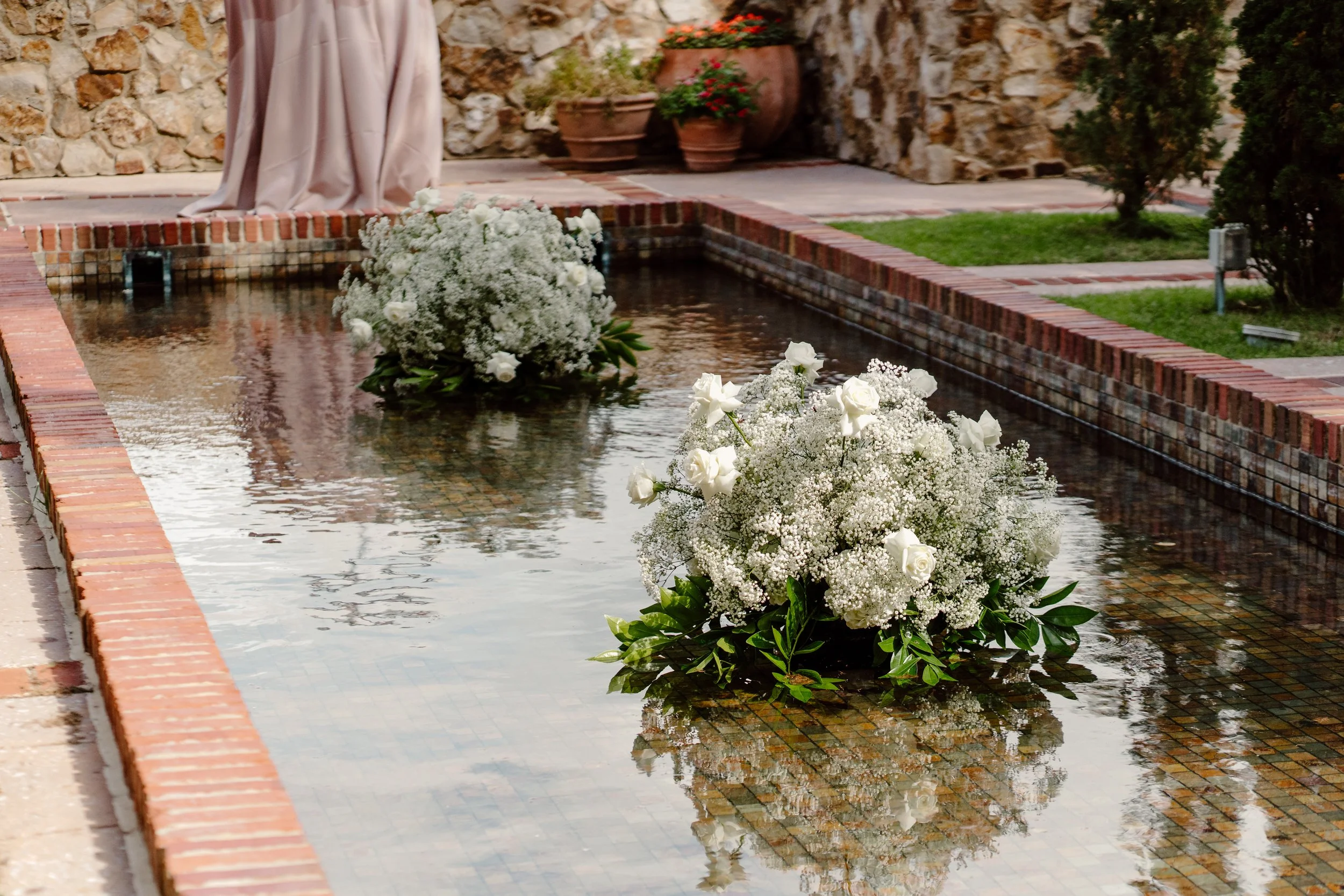 White flowers floating on a narrow water feature surrounded by brick and stone landscaping.