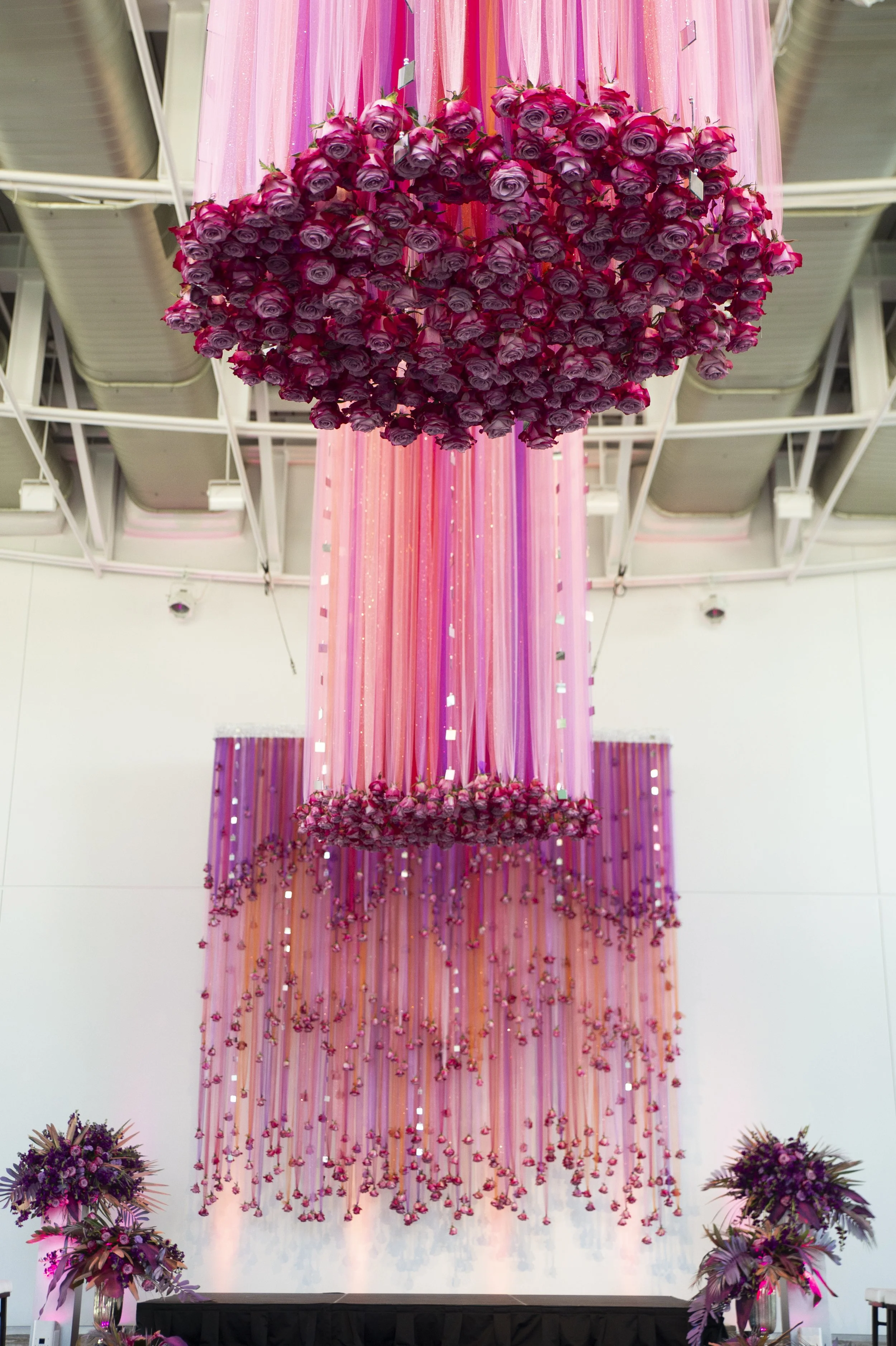 Decorative floral arrangement with pink roses and purple flowers hanging from the ceiling, with pink and purple drapes creating a backdrop.
