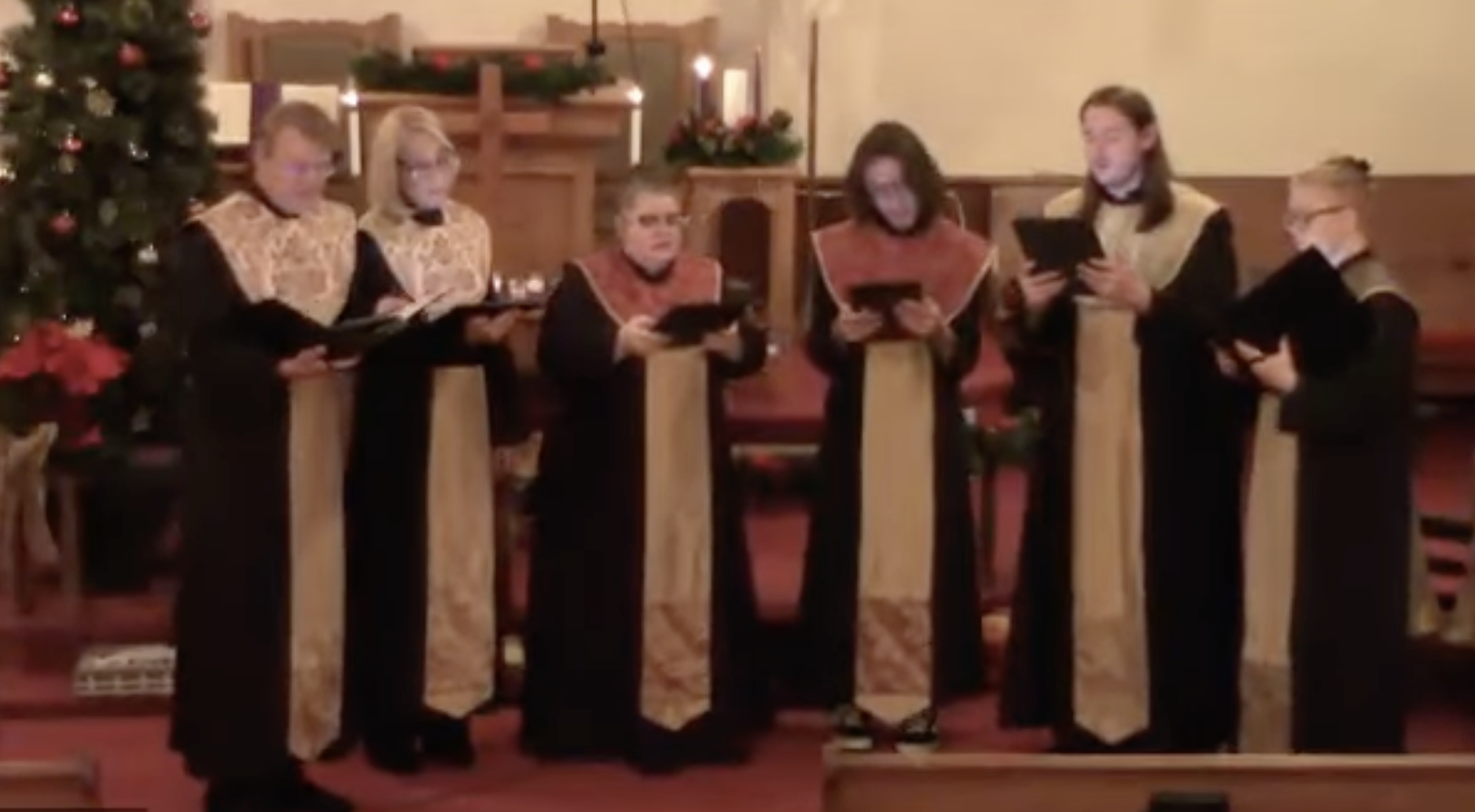 Members of Asheville Vocal Ensemble singing in a church decorated for Christmas with trees, candles, and poinsettias.