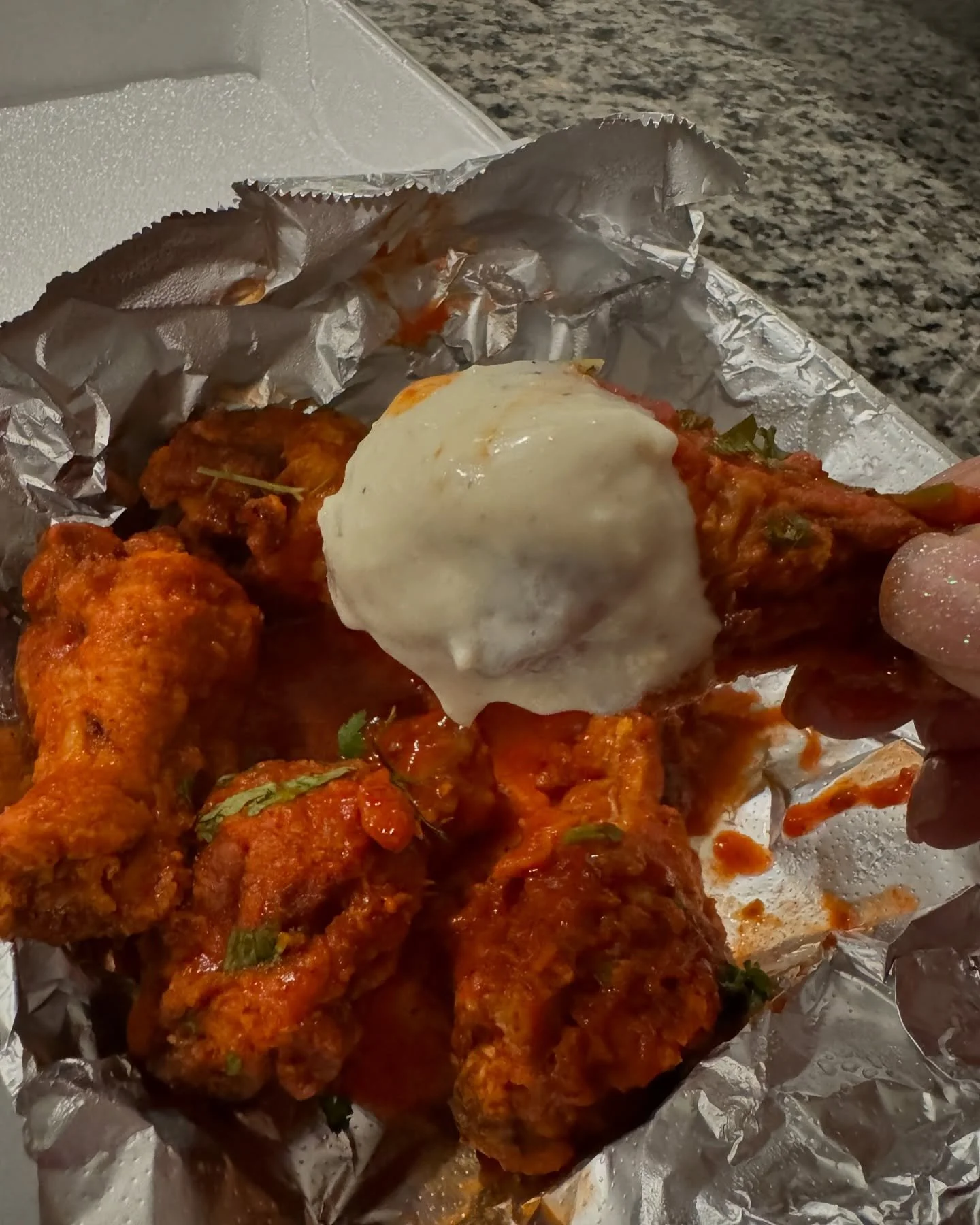 Close-up of spicy chicken drumsticks and a poached egg on foil and a paper towel with a granite countertop in the background.
