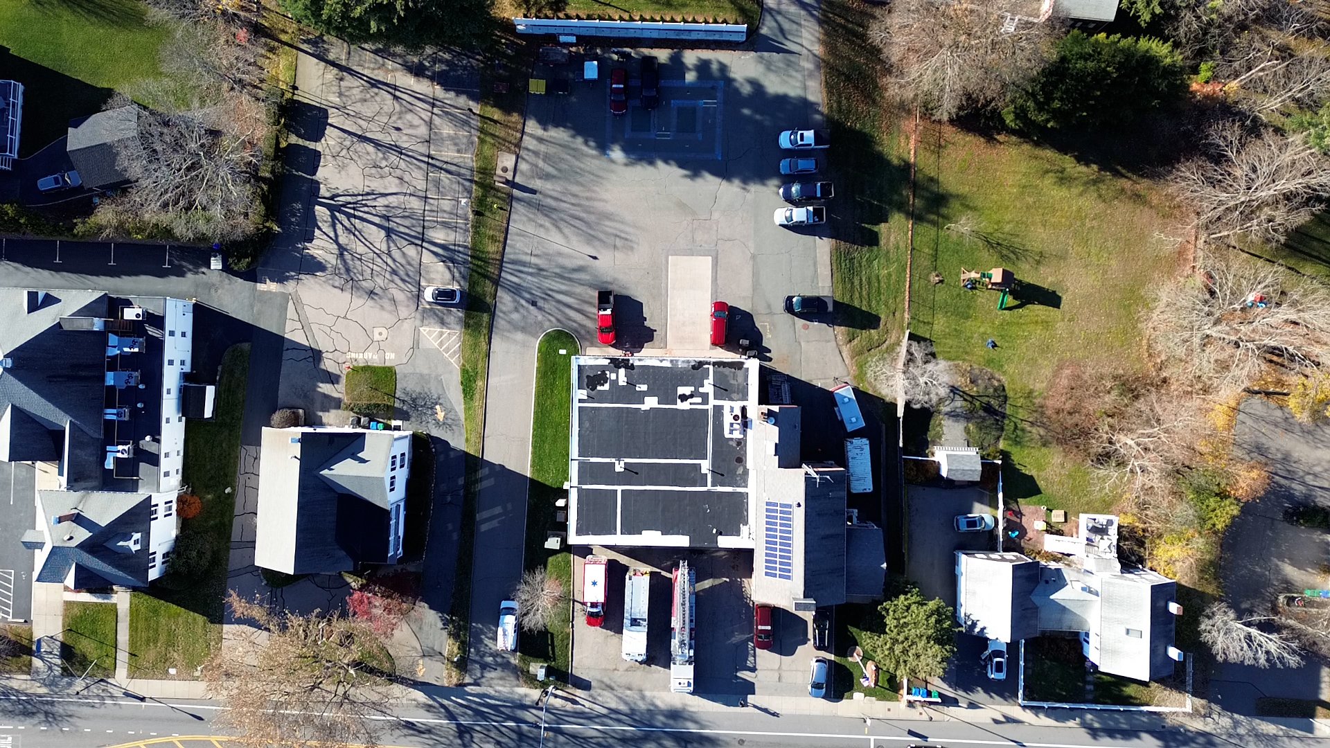 Aerial view of a parking lot surrounded by residential houses and trees with shadows cast on the ground.