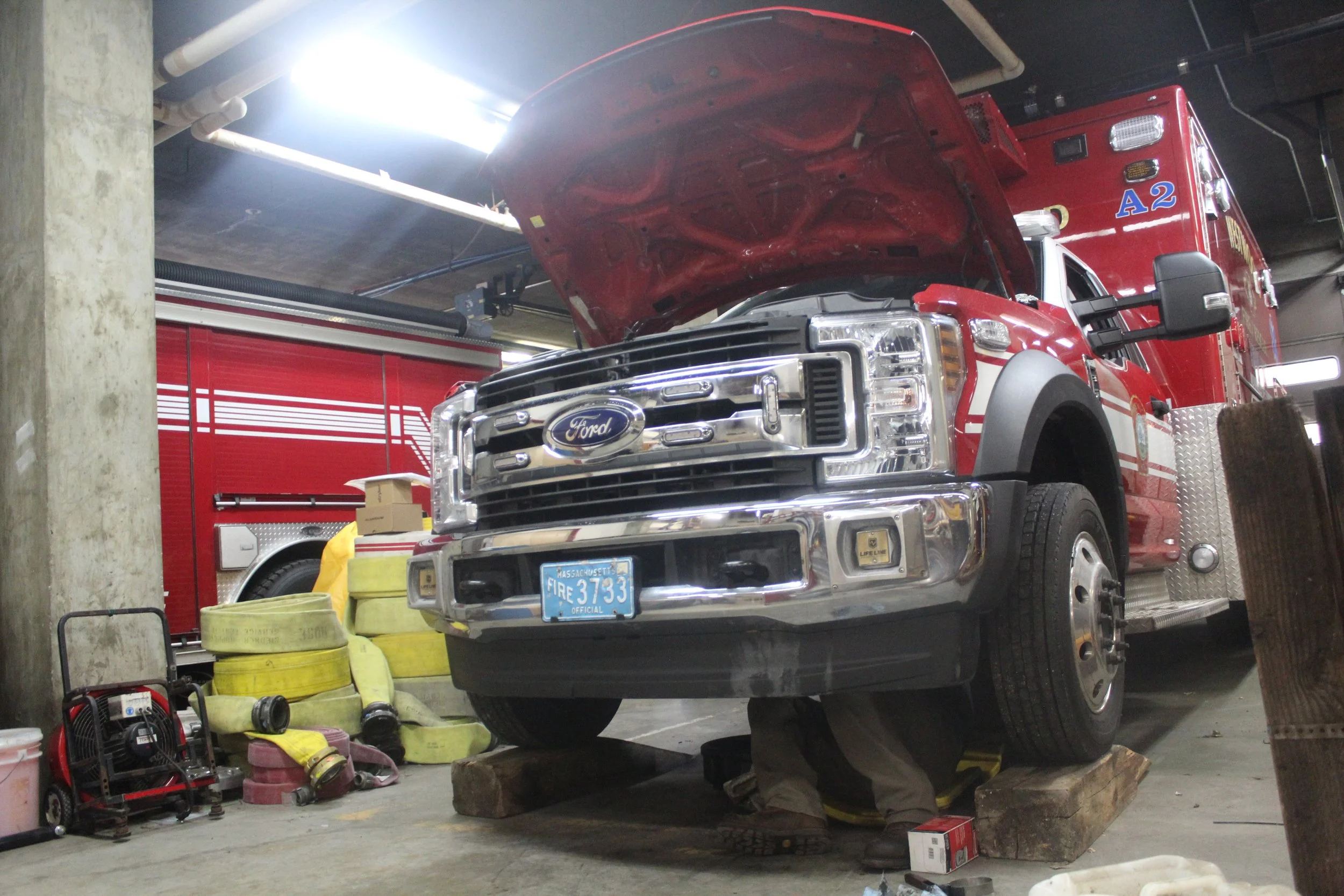 A fire apparatus with its hood open and being worked on in the mechanic's bay