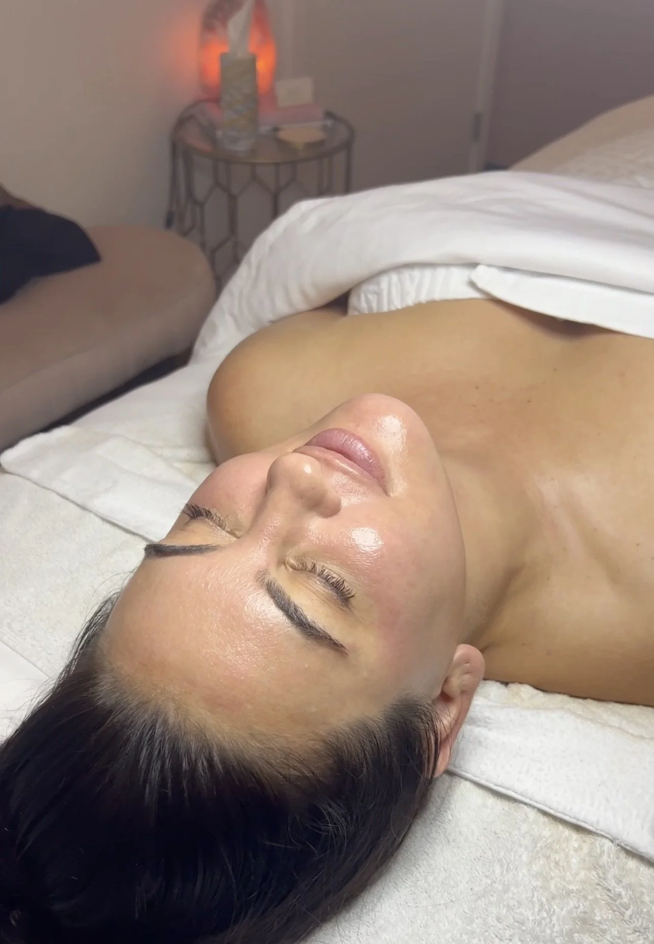 A woman lying on a massage table with her eyes closed and a towel covering her lower body.