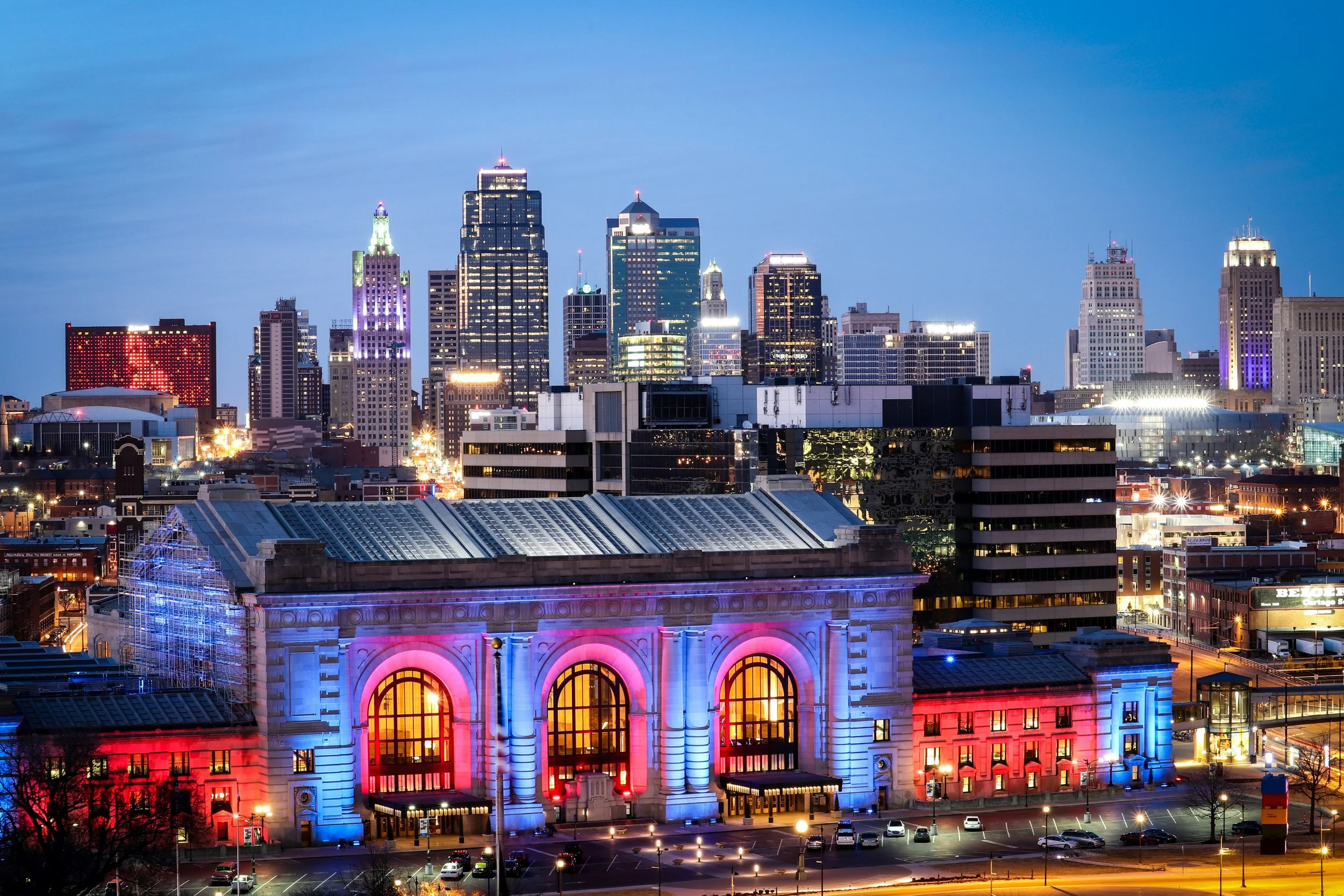 Night cityscape of downtown with illuminated skyscrapers and a historic building with colorful lighting in the foreground.