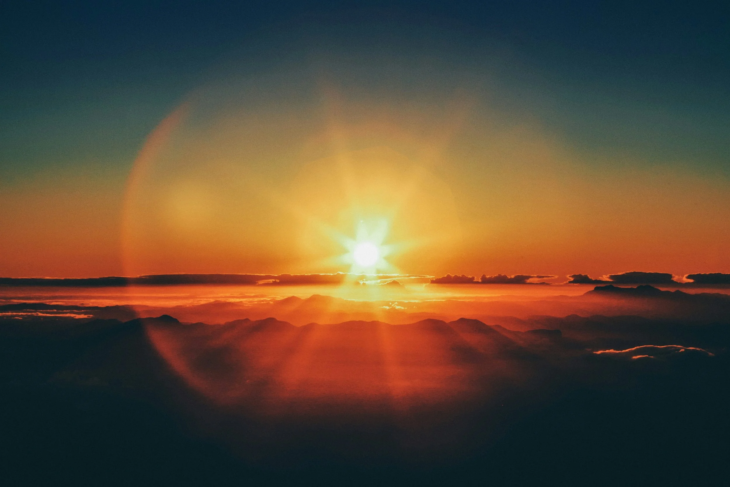 Sunset over mountainous landscape with a vibrant orange and yellow sky, creating a lens flare effect.