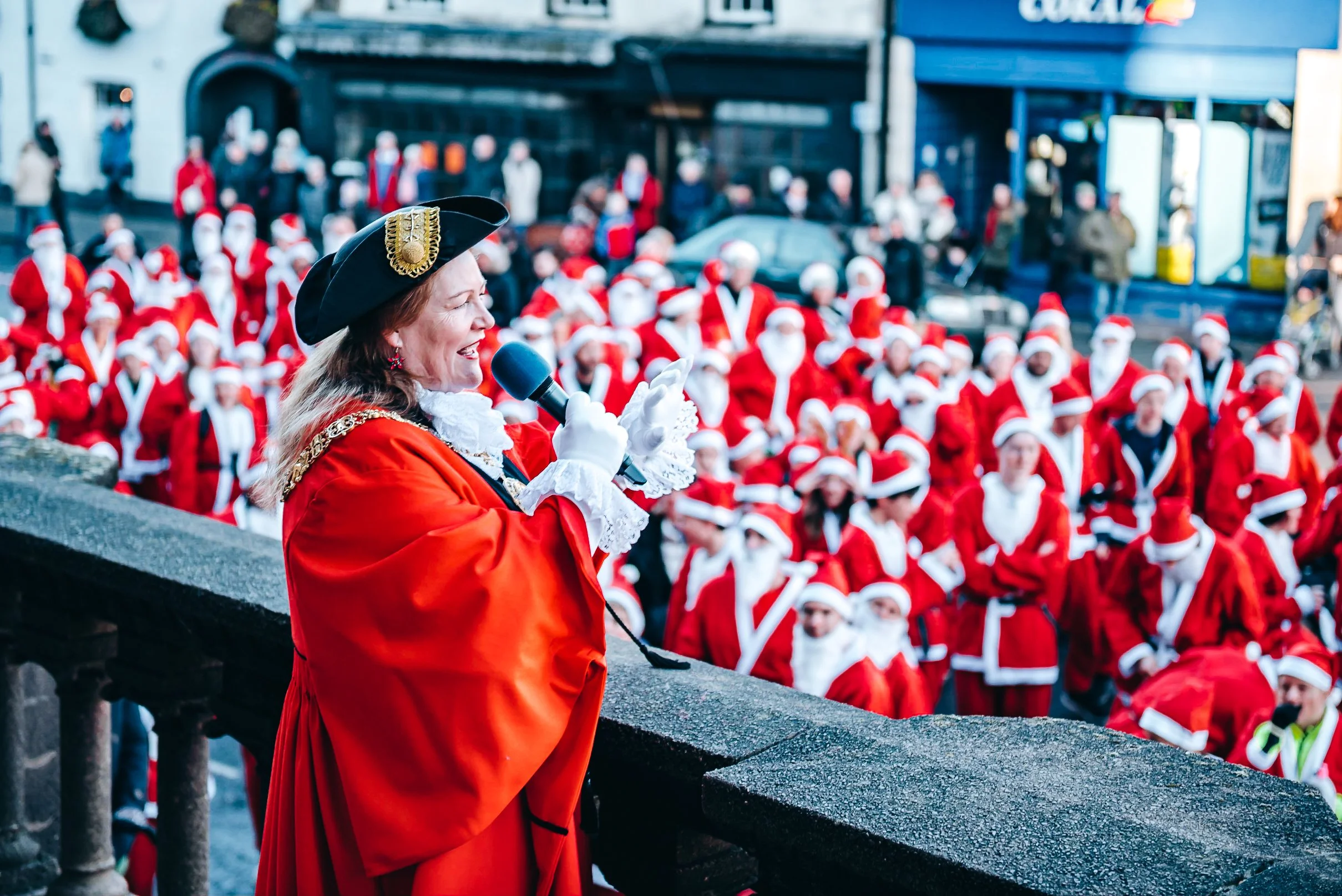 The Mayor of Winchester addressing hundreds of festive runners gathered for the annual city center Christmas Santa Fun Run. Vibrant community festival and seasonal event photography by Will Bailey.