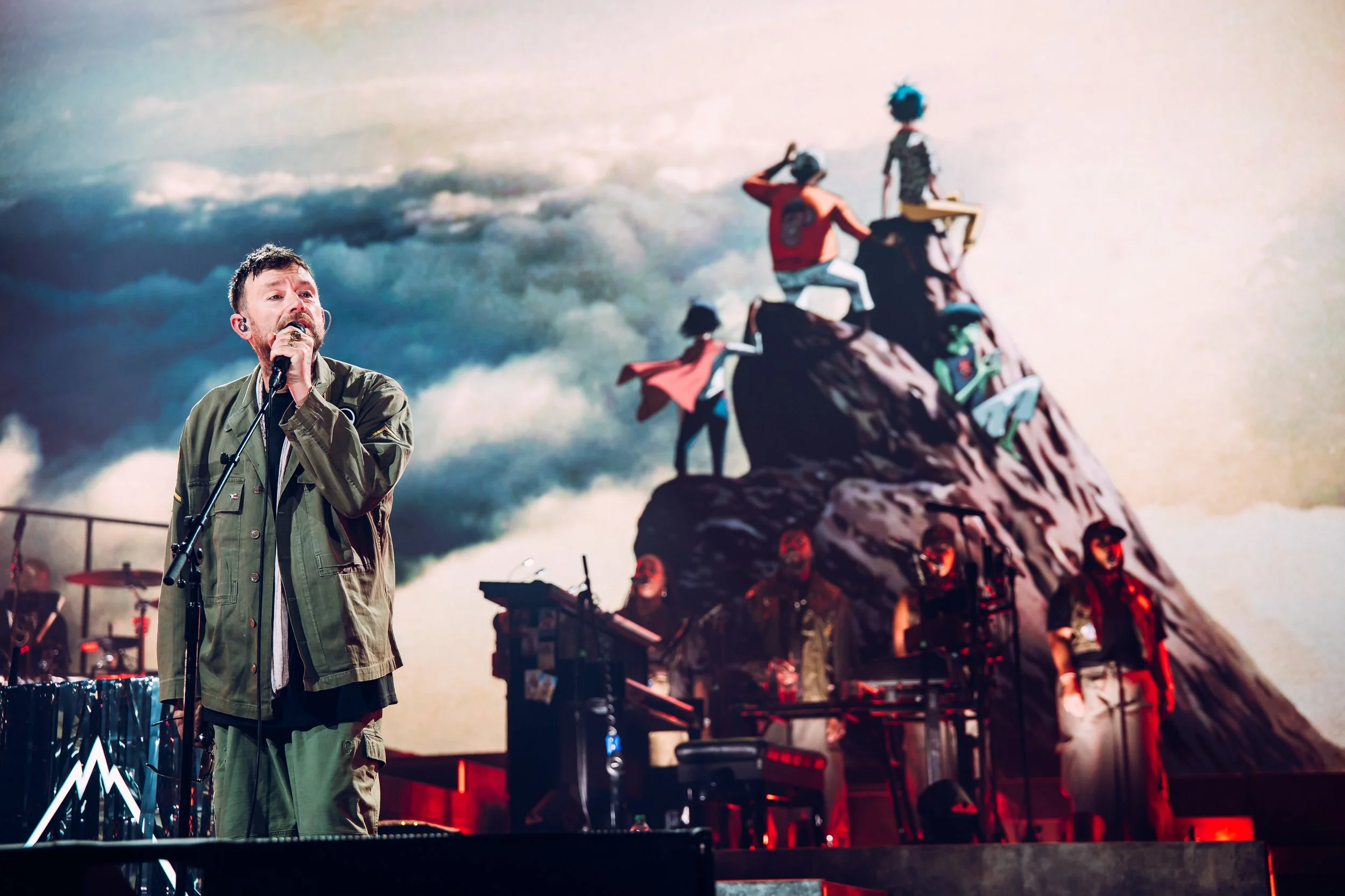 Frontman Damon Albarn of Gorillaz performing live on stage against a giant digital backdrop featuring iconic animated band visuals at the Cardiff International Arena. High-profile stadium act and professional live music tour photography by Will Baile