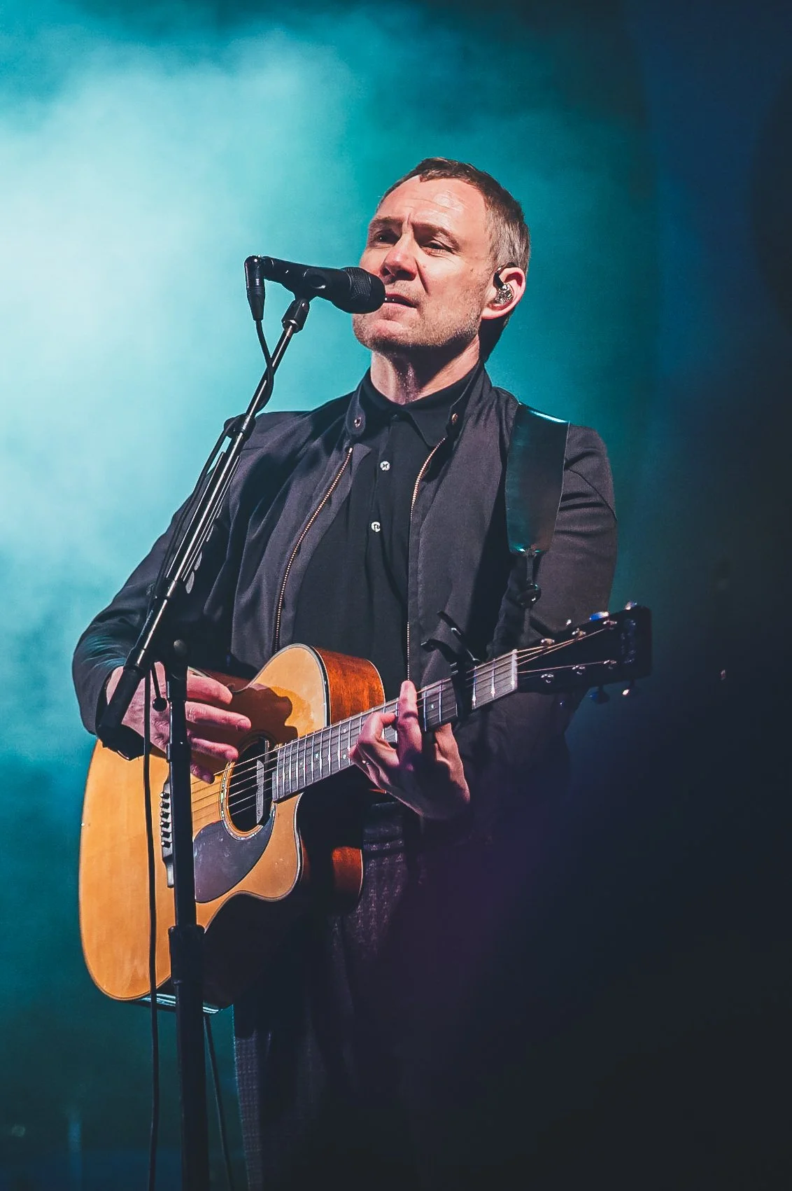 Singer-songwriter David Gray performing an emotional acoustic set with his guitar under a blue spotlight at Pub in the Park in Marlow, Buckinghamshire. Professional outdoor food and music festival stage photography by Will Bailey.