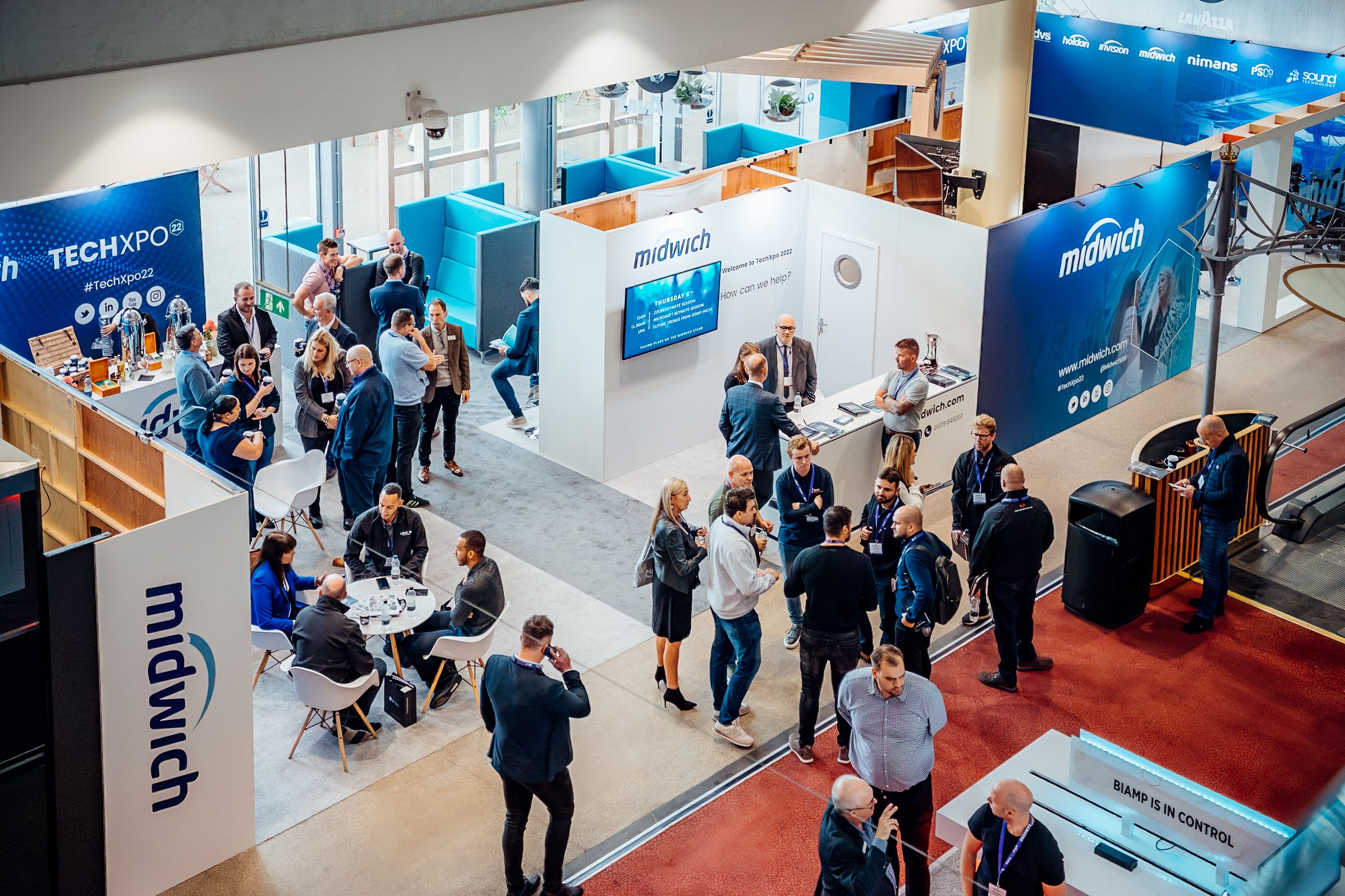 An elevated view of corporate exhibition stands and active B2B networking at the Midwich Tech Xpo, hosted at Ascot. Professional trade show and convention photography by Will Bailey.