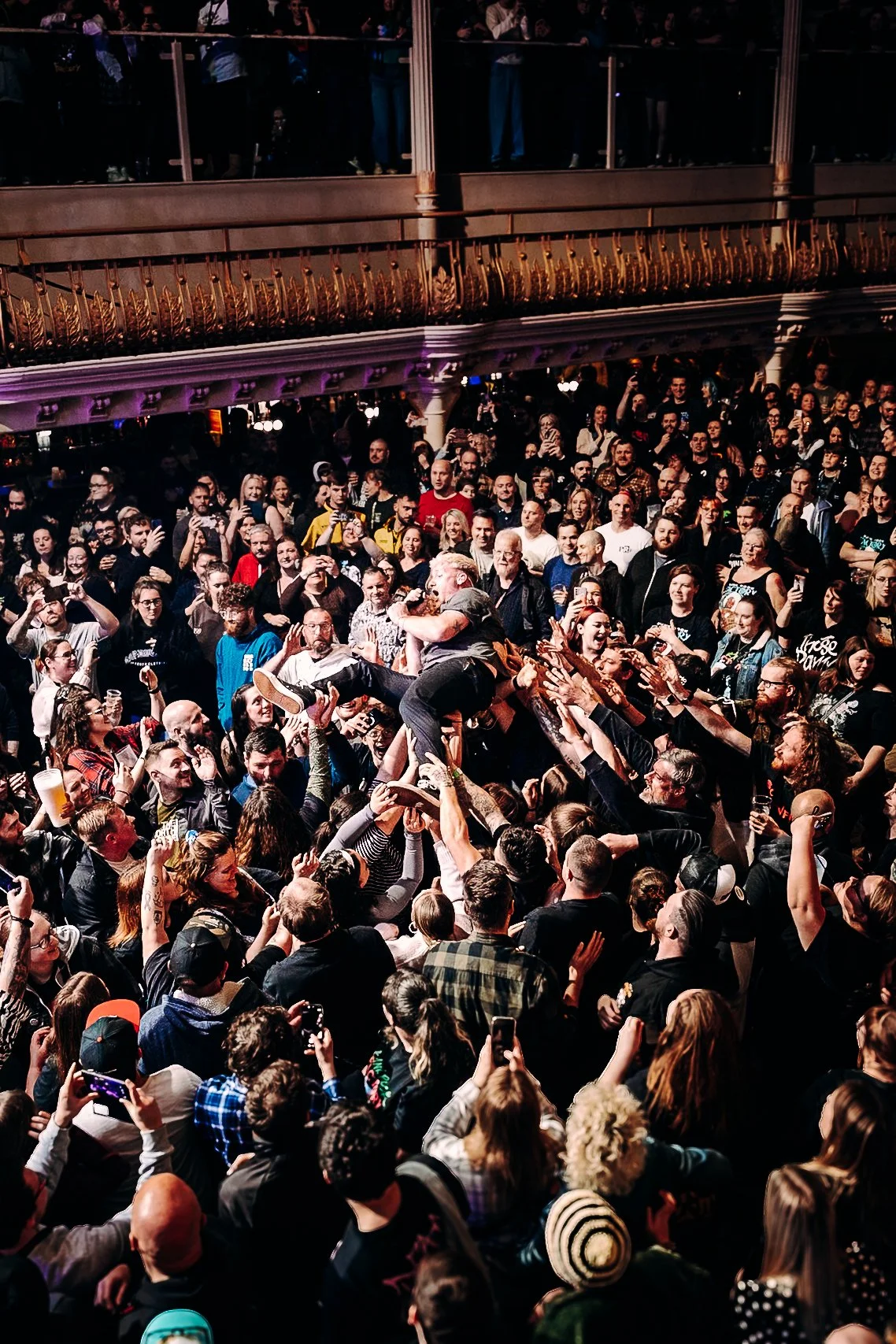 A high-angle shot capturing a packed room as the vocalist of pop-punk band The Bottom Line crowd-surfs through fans at the O2 Academy Bournemouth. Immersive nationwide music tour documentary photography by official tour photographer Will Bailey.